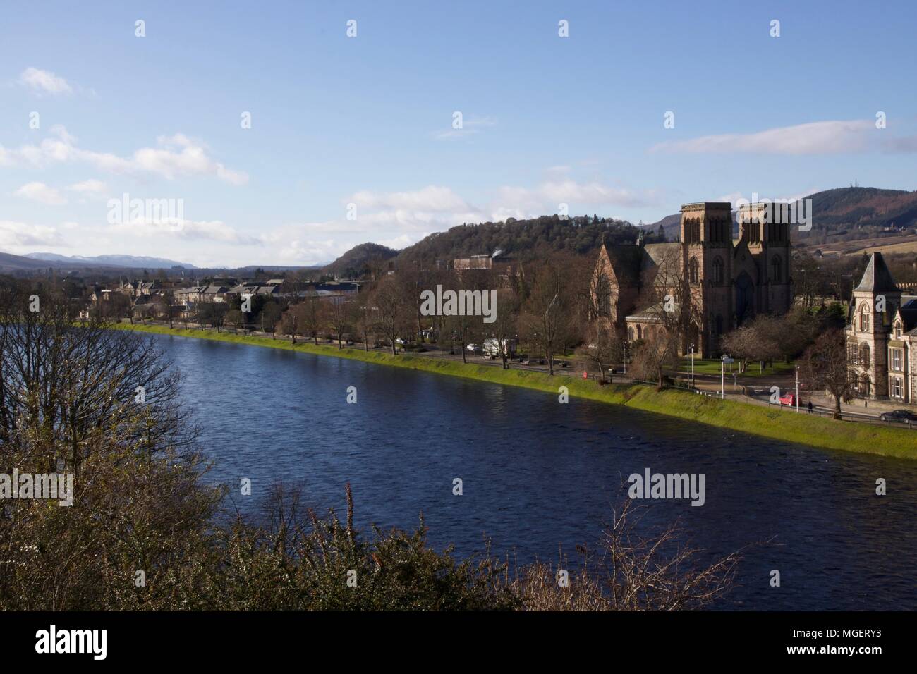 A cathedral in Inverness runs along the Scottish city river on a sunny day with blue skies and green trees in the foreground Stock Photo