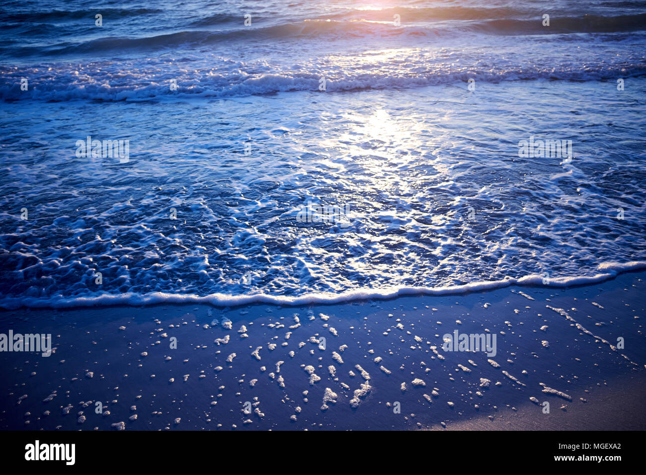 Glowing sunset at blue hour on Anna Maria Island, Florida with a low angle view of gentle surf lapping the beach and reflection of the sun on the wate Stock Photo