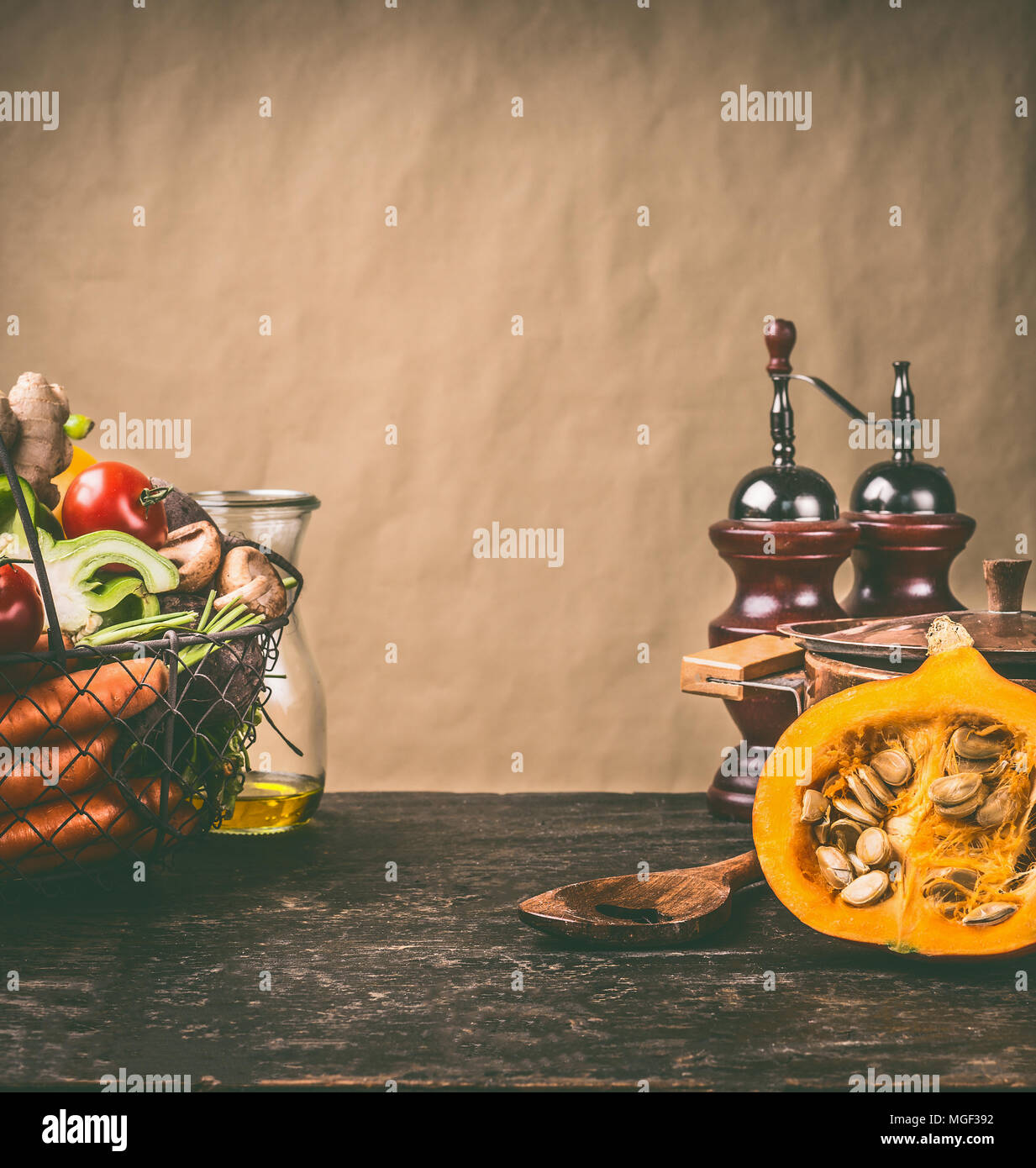 Pumpkin on kitchen table with cooking pot and basket of vegetables ingredients at rustic wall background, front view. Healthy vegetarian  food and eat Stock Photo