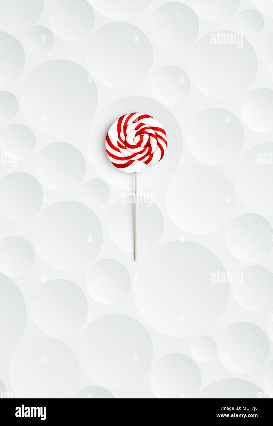 Red striped and spiral shaped lollipop on white and bubble textured background Stock Photo