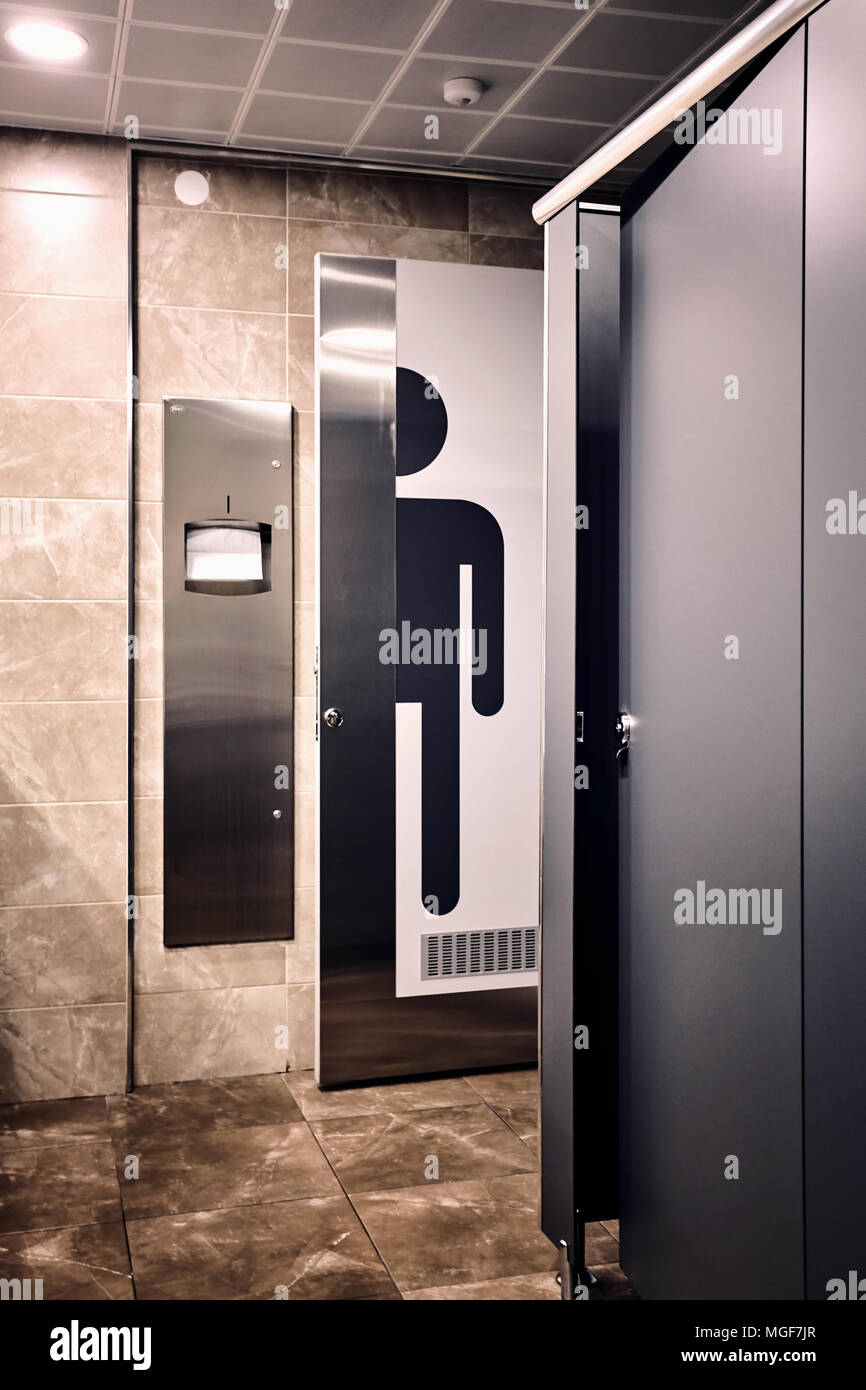 An interior shot of a men's restroom toilette. A big man sign on the toilette door next to the towel rack. Stock Photo