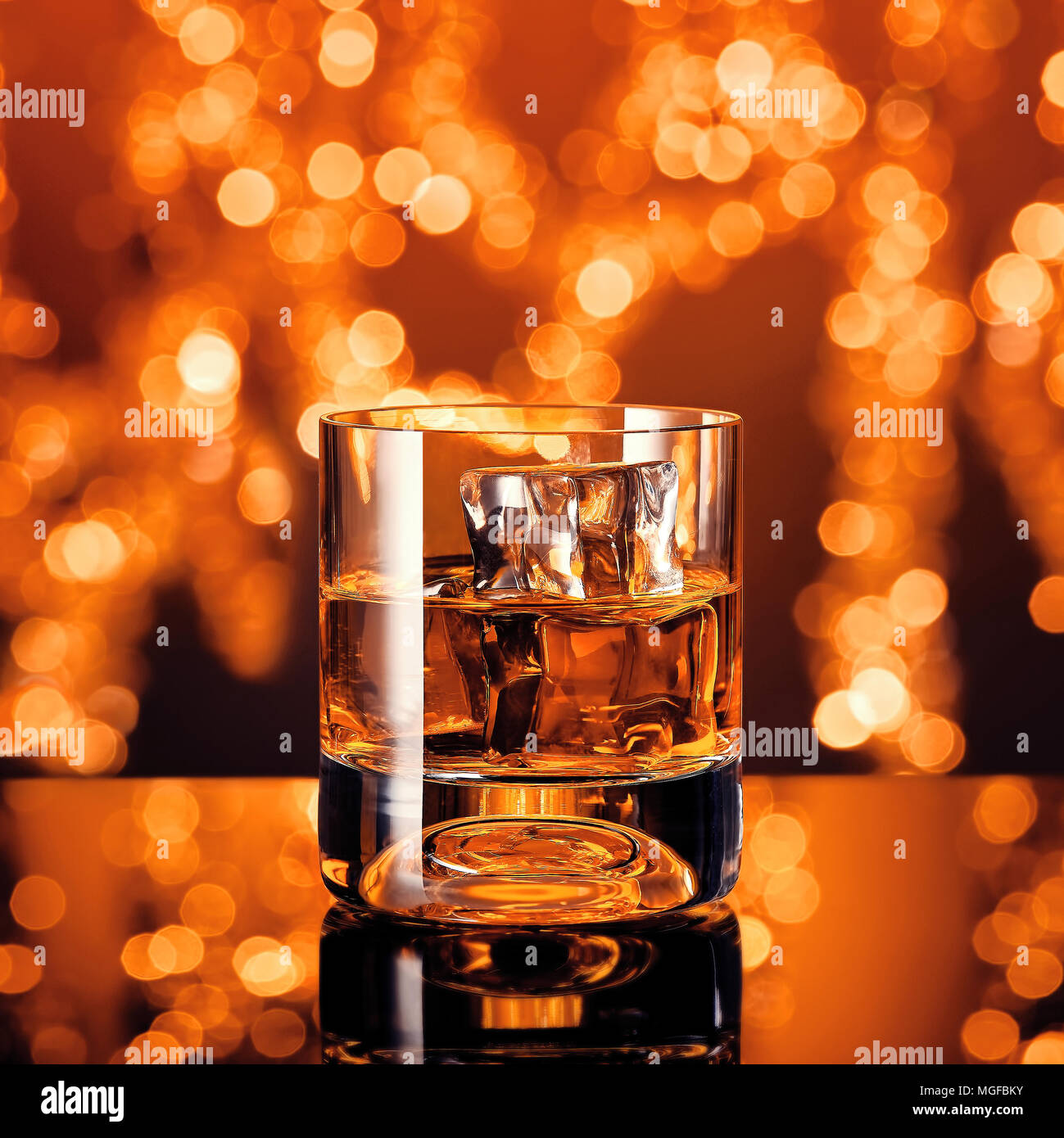 Whiskey glass with ice cubes on blurry Christmas lights background Stock Photo