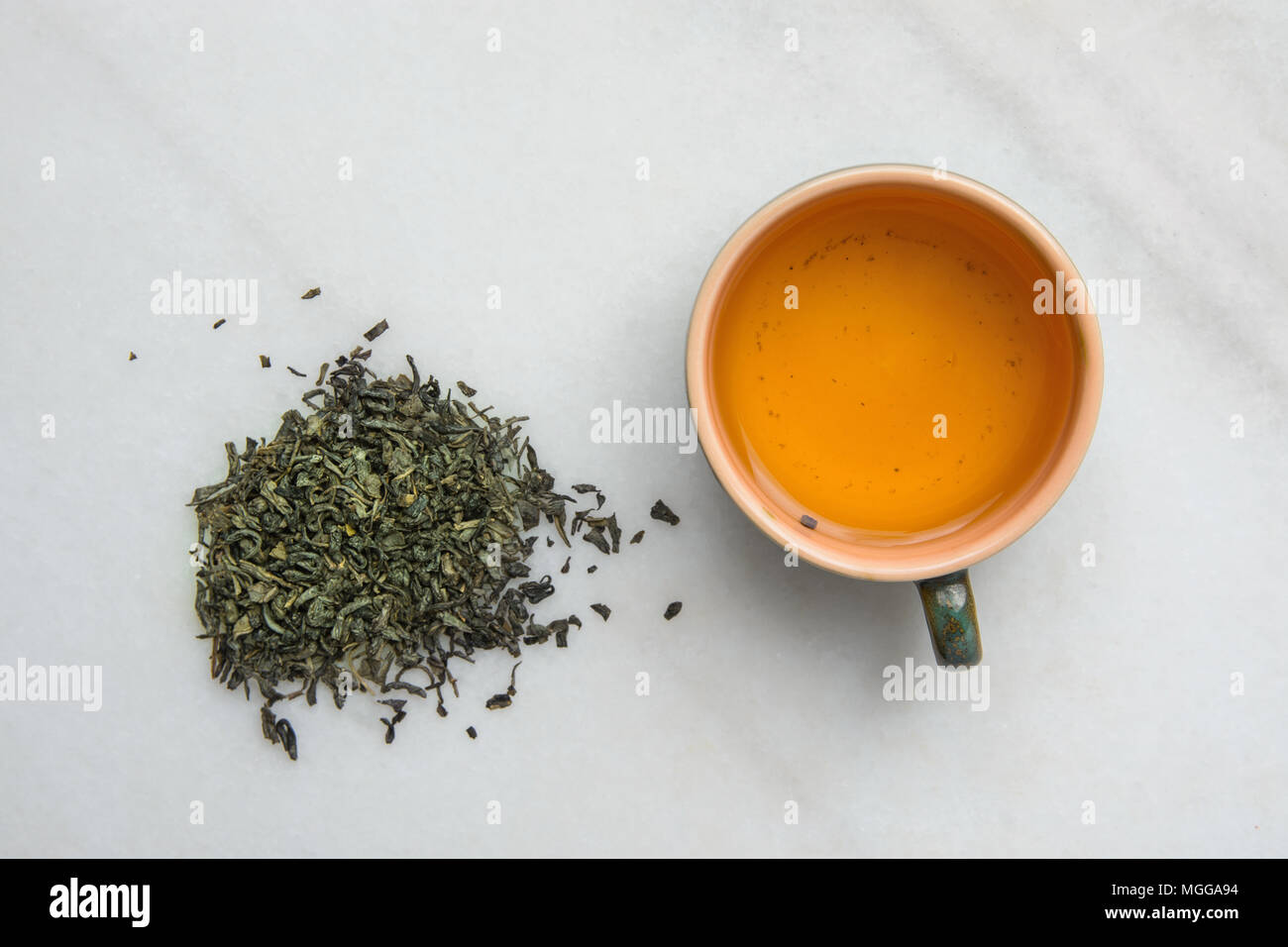 Brewed Green Tea in Ceramic Cup. Loose Leaves Scattered on White Marble Stone Background