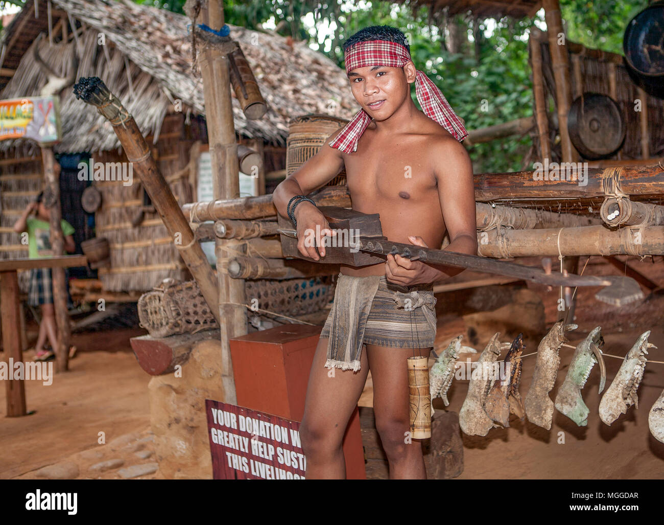 A teenage Palawano tribesman plays a native Filipino guitar, paglong, to entertain tourists visiting the Palawan Eco Butterfly Garden and Tribal Villa Stock Photo
