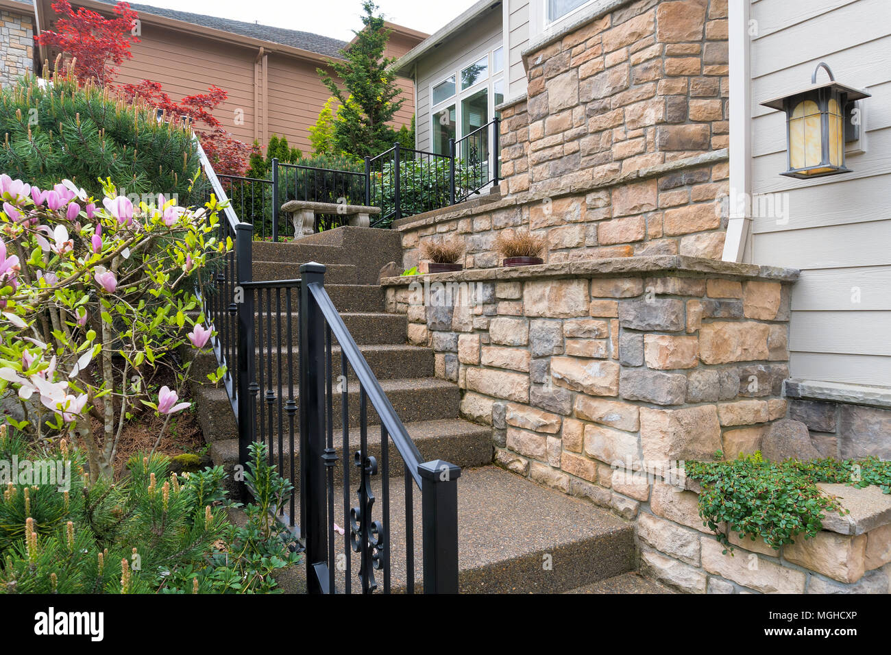 House front entry with concrete stairs iron rod railings stone wall planter siding by frontyard garden Stock Photo