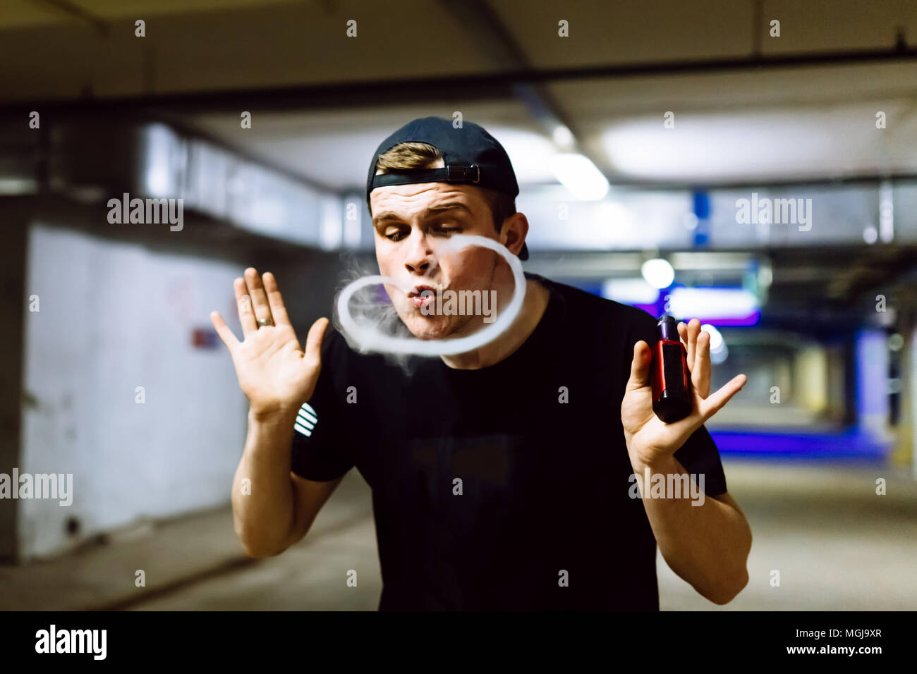 Man in cap smoke an electronic cigarette and releases clouds of vapor performing various kind of vaping tricks Stock Photo