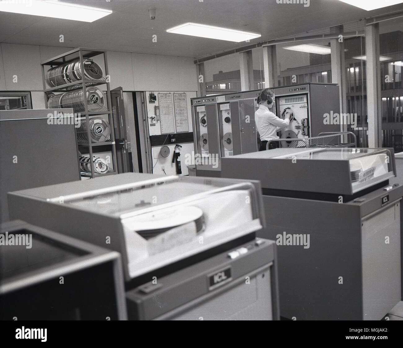 1970s,  young female working in an internal office area filed with large ICL mainframe data processors or early computers. ICL was a British computer company that supplied these types of hardware machines to the UK public sector and other such large employers and was supported by the UK government in an attempt to create a rival to the american computer giant, IBM. Stock Photo