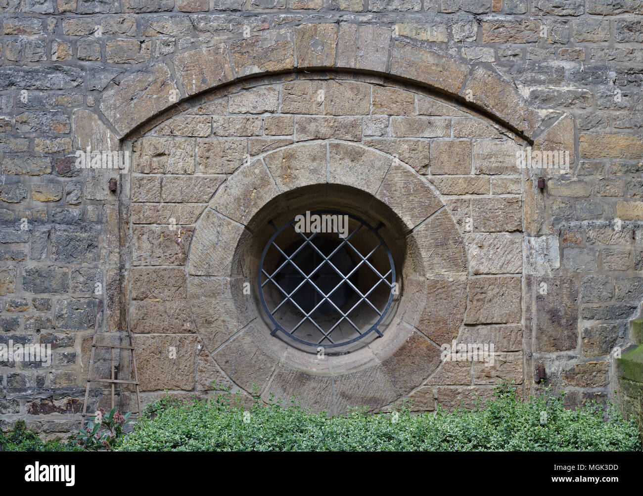 Ancient sandstone wall with arch and barred round window Stock Photo