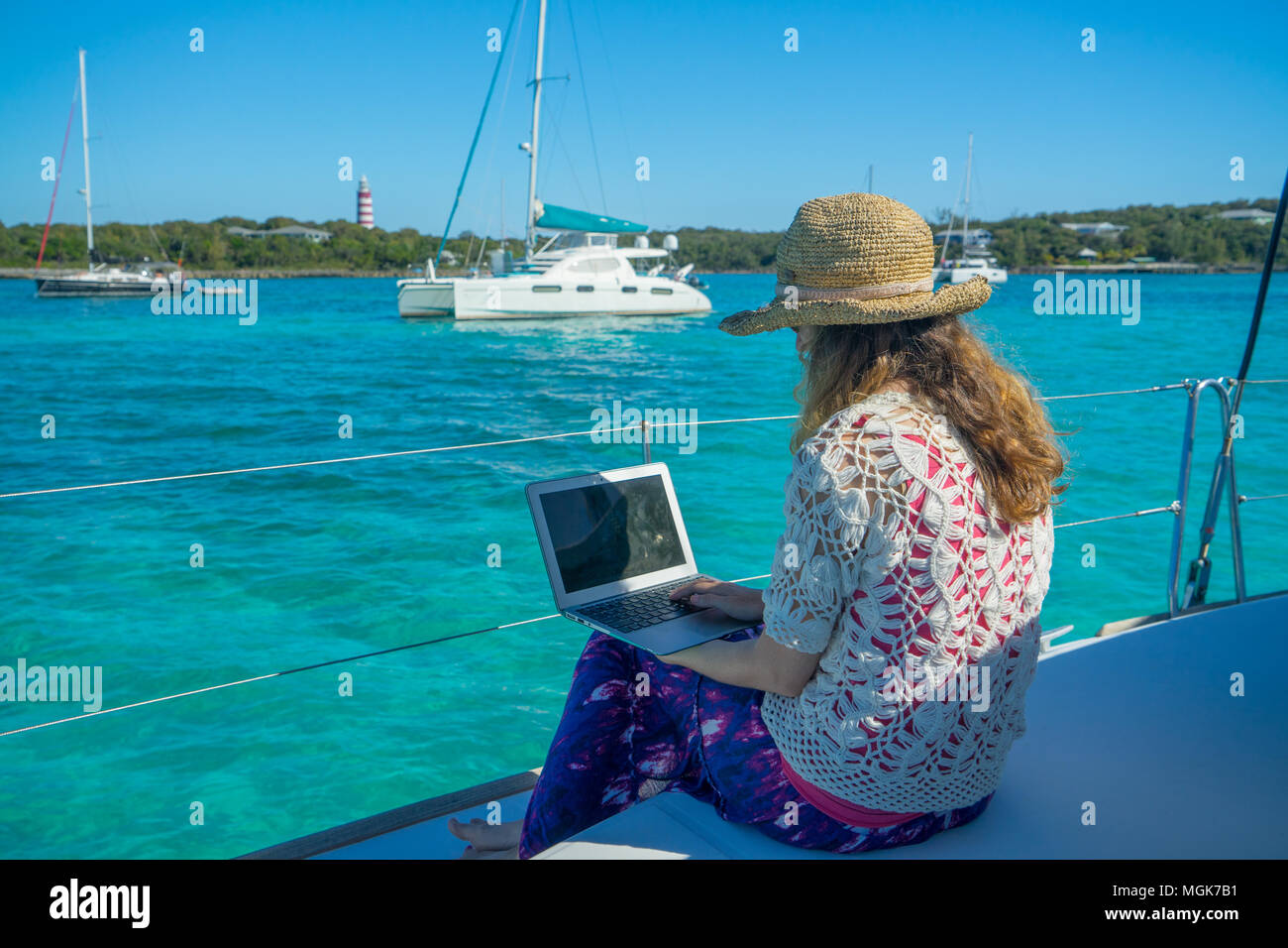 young woman in sun hat and sunglasses works on a laptop from the bow sun works stock