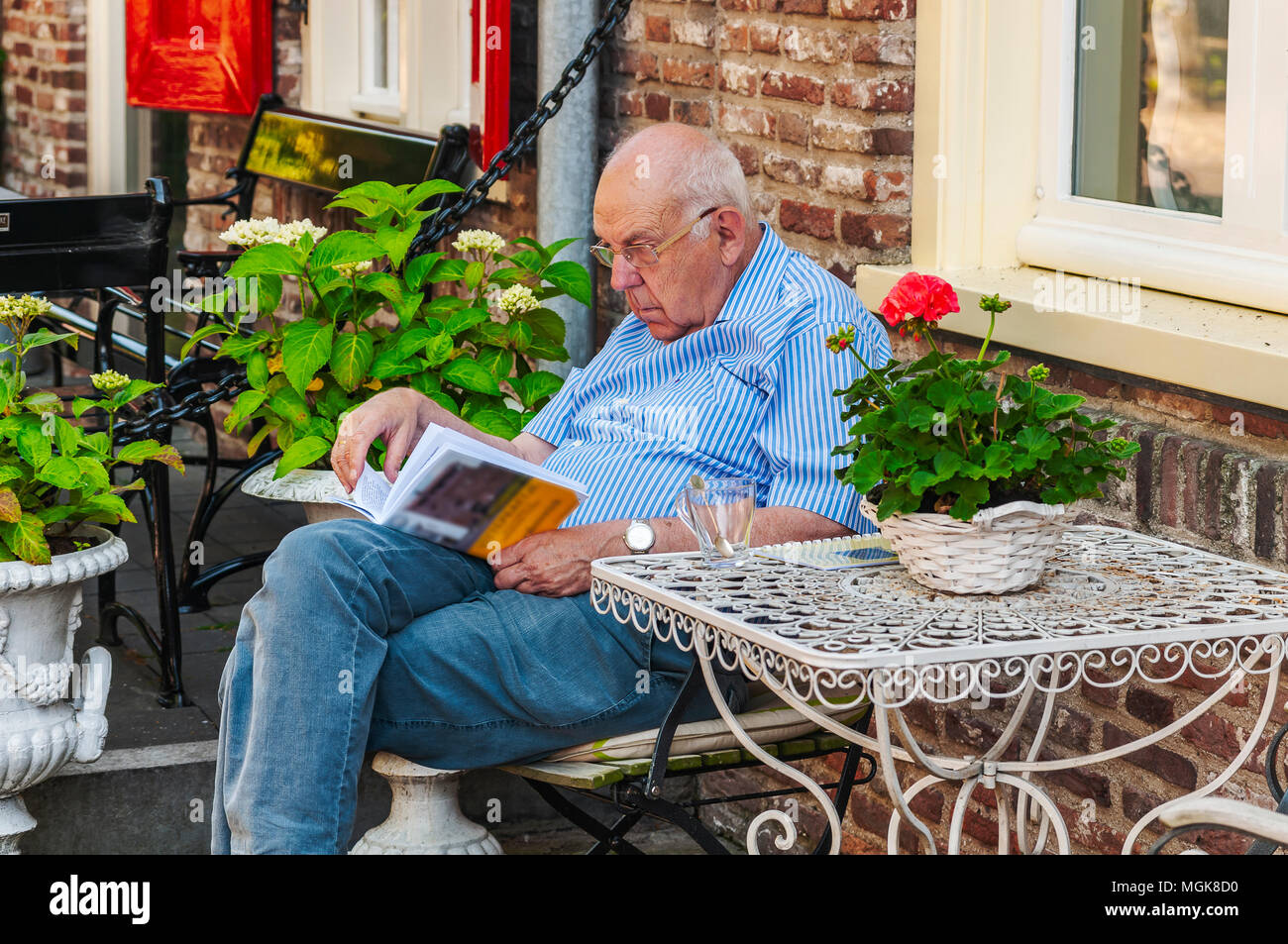 an elder man is reading his book in front of a house Stock Photo