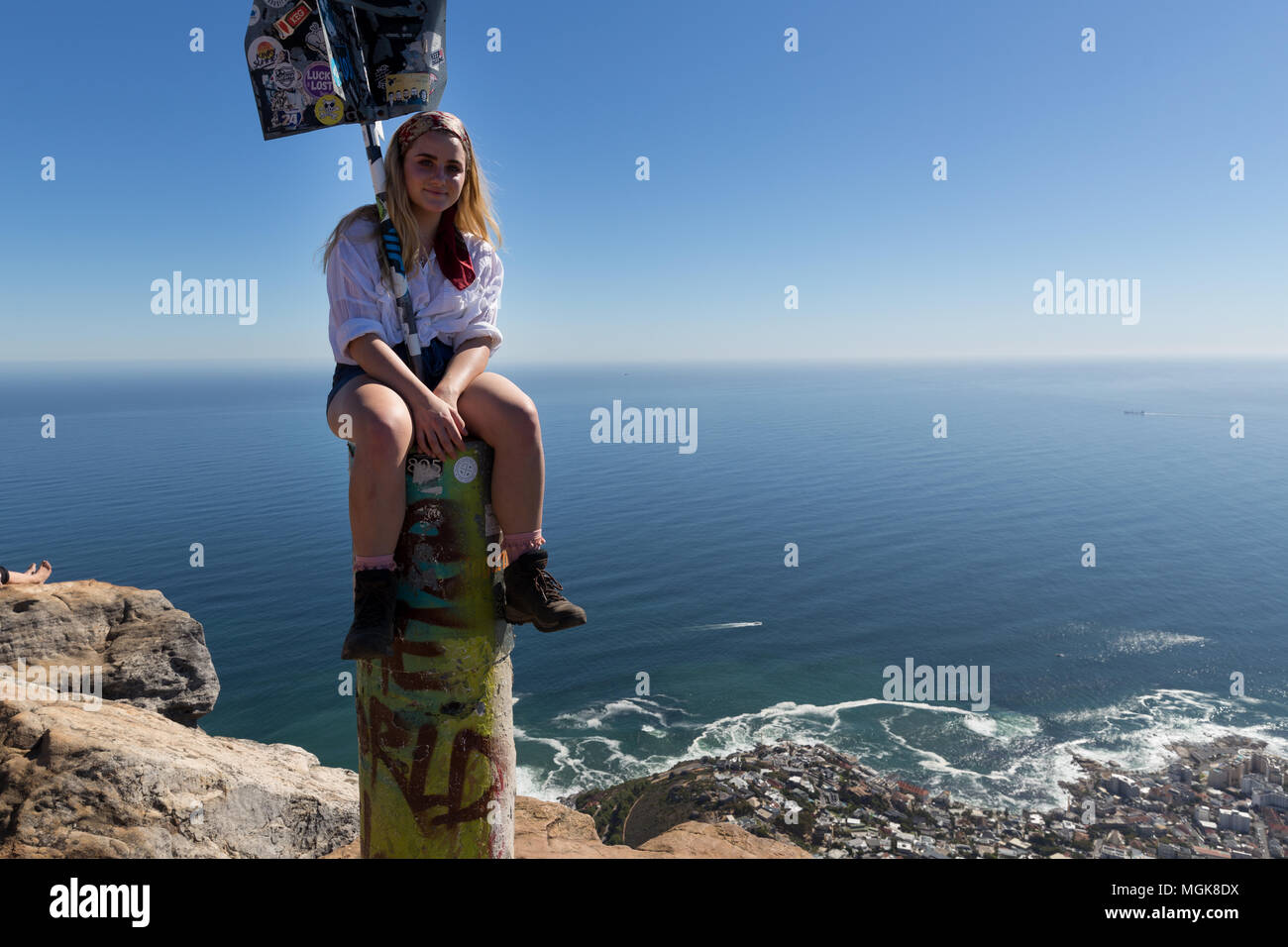 A pretty woman sits on top of the marker after hiking up Lion's Head, Cape Town Stock Photo