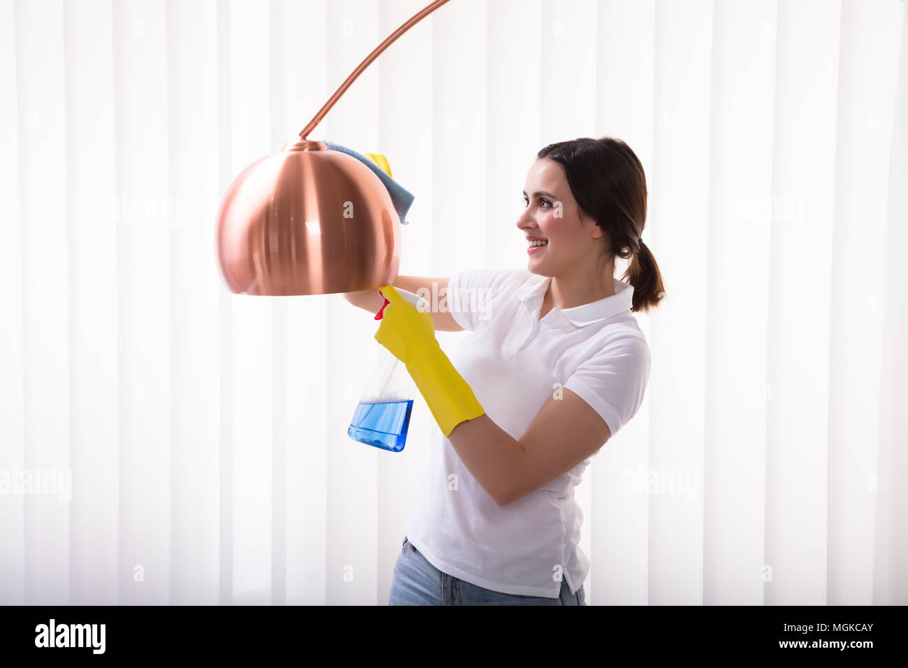 Close-up Of A Smiling Young Woman Cleaning Electric Lamp With Spray At Home Stock Photo