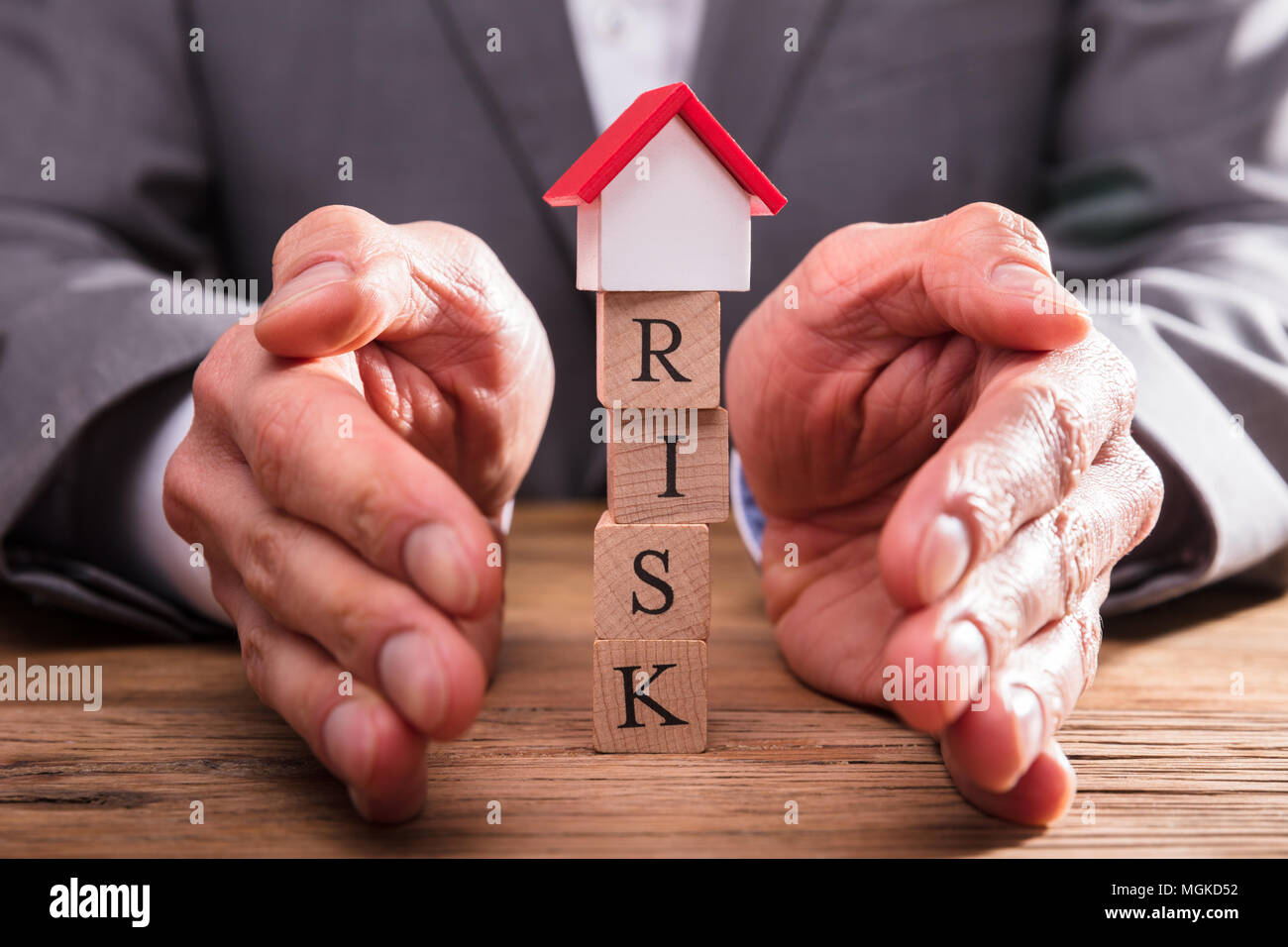 Businessperson's Hand Protecting Risk Wooden Blocks With House Model ...