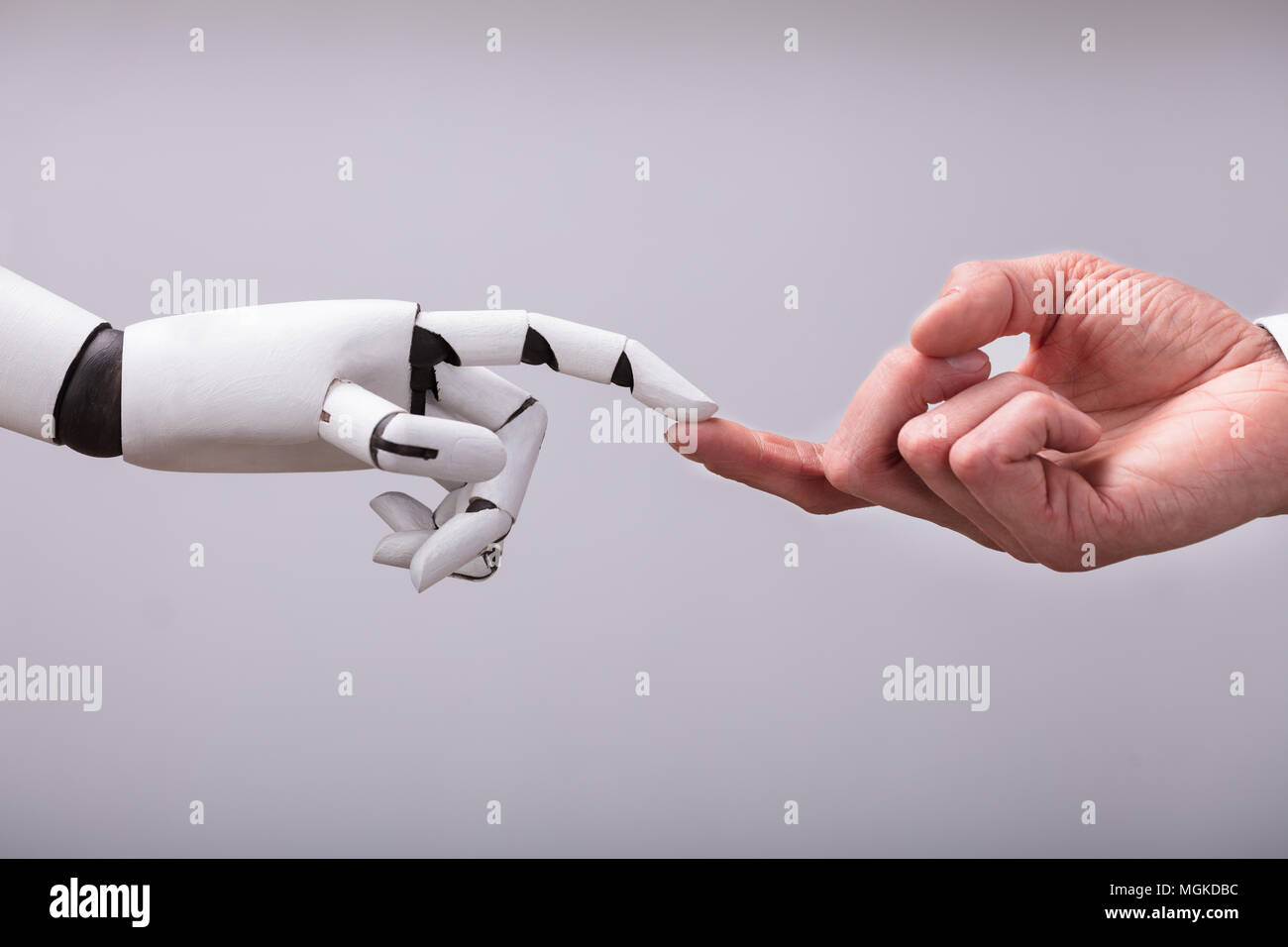 Robot Touching Human Finger Against Gray Background Stock Photo