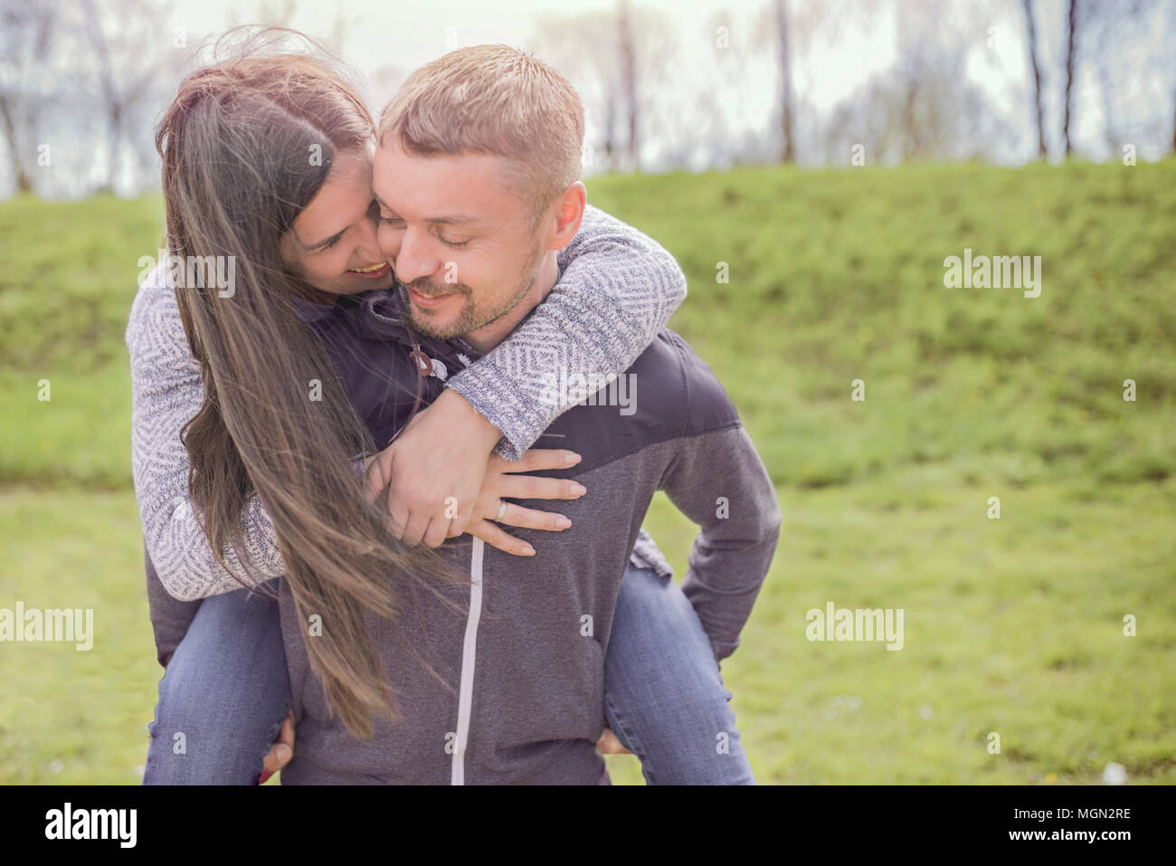 Smiling couple in love outdoors. Beautiful young couple enjoying piggyback in sunny day and smiling while playing outdoors Stock Photo