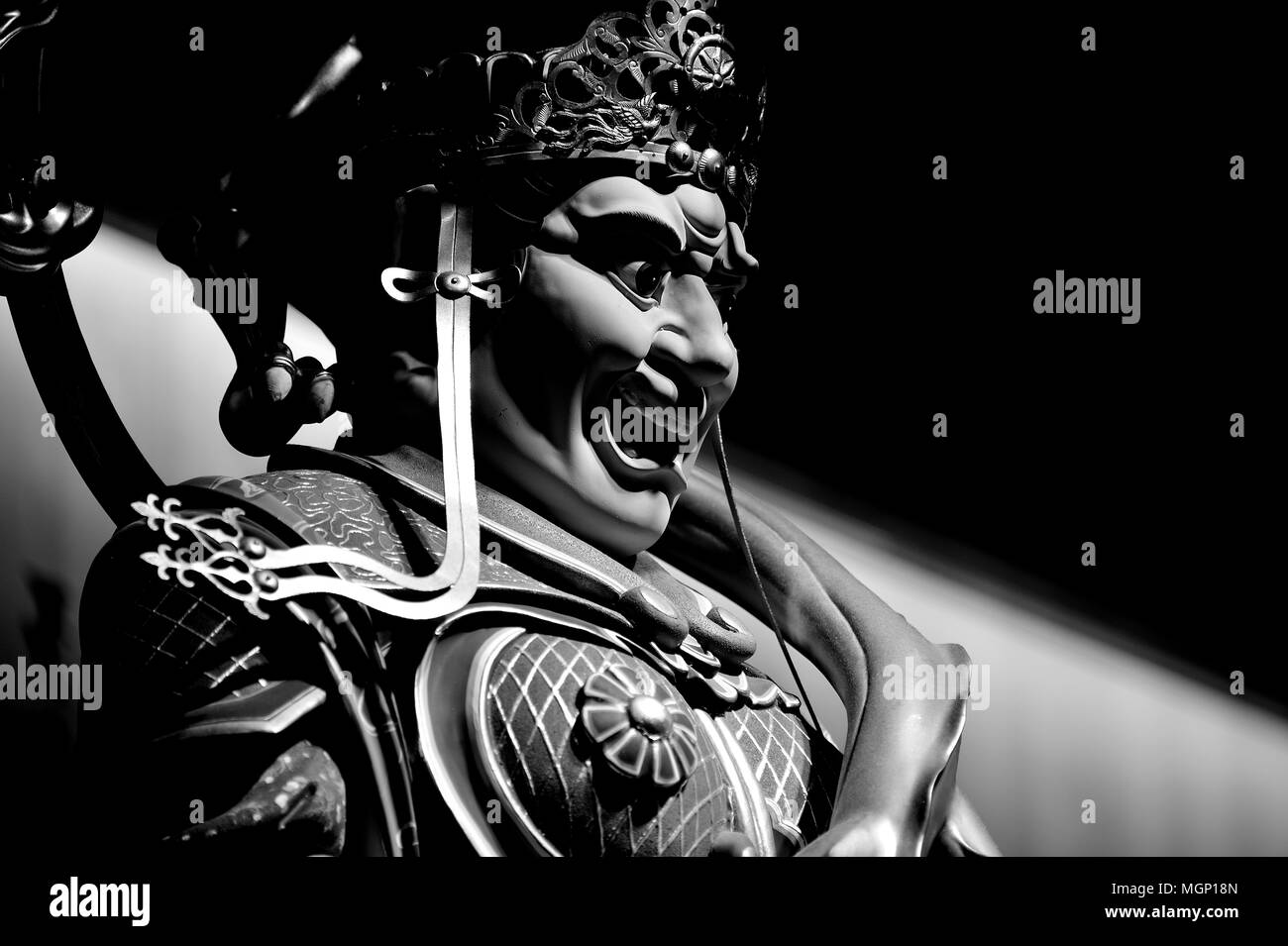 Close up of ancient stone statue of a fierce Chinese Buddhist temple guardian in monochrome with strong shadows as Asian art with space for copy Stock Photo