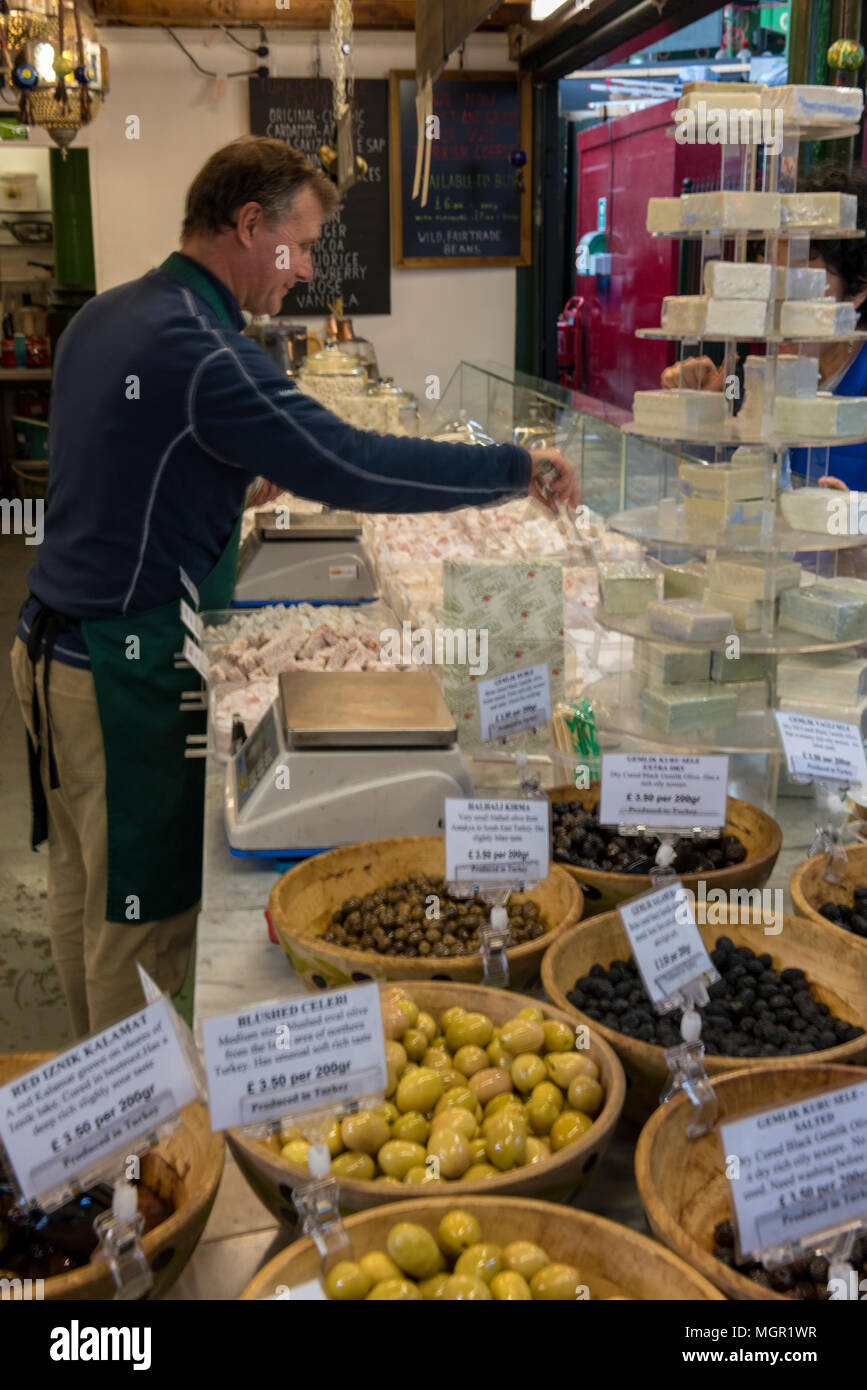 a stall holder or market trader selling fresh olives and continental speciality cheeses at a stall on borough market in london. high quality foods. Stock Photo