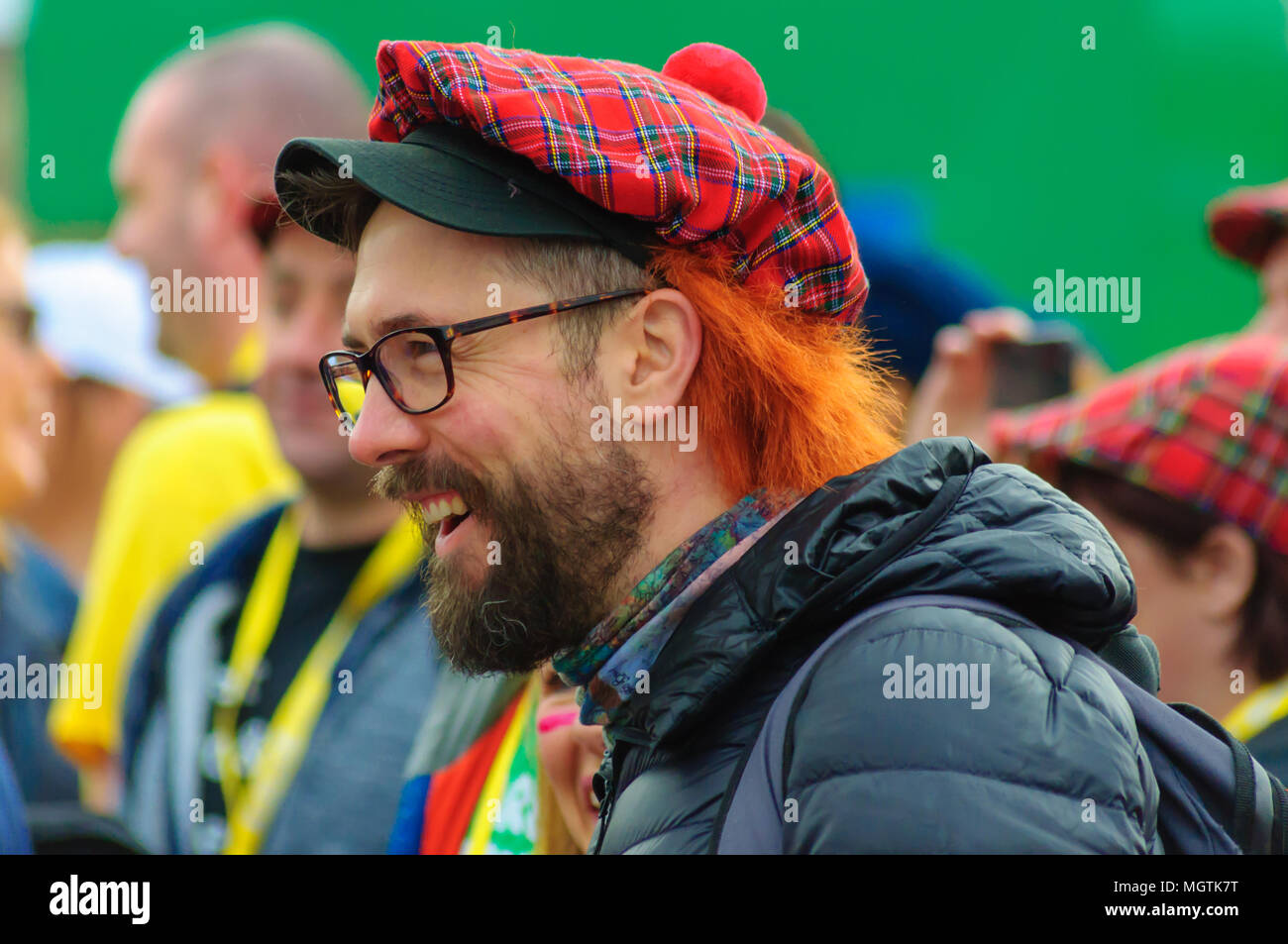 Glasgow, Scotland, UK. 29th April, 2018. Kiltwalk Glasgow 2018, a charity event where walkers have three distances to choose from, a Mighty Stride (23 miles), a Big Stroll (14 miles) or the Wee Wander (6 miles). This year involved 10,000 walkers and raised two million pounds for 600 charities. Pictured a smiling man with beard and glasses wearing a tartan hat with ginger wig aka see you jimmy hat. Credit: Skully/Alamy Live News Stock Photo