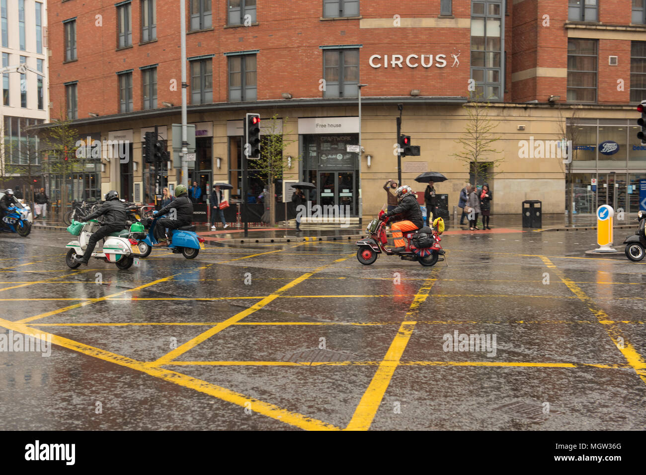 Group of scooter riders navigating a wet city intersection on a rainy day in front of Circus restaurant, Sheffield city centre, South Yorkshire, Engla Stock Photo