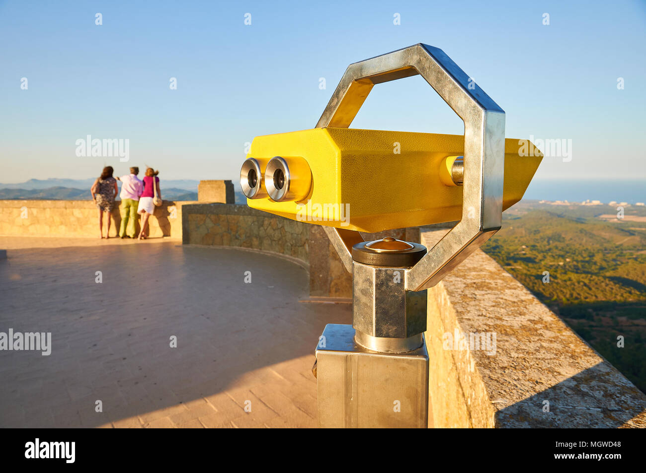 Yellow telescope viewer and 3 tourists looking at the distance to the scenic view at Sant Salvador Santuary (Felanitx, Majorca,Balearic Islands,Spain) Stock Photo