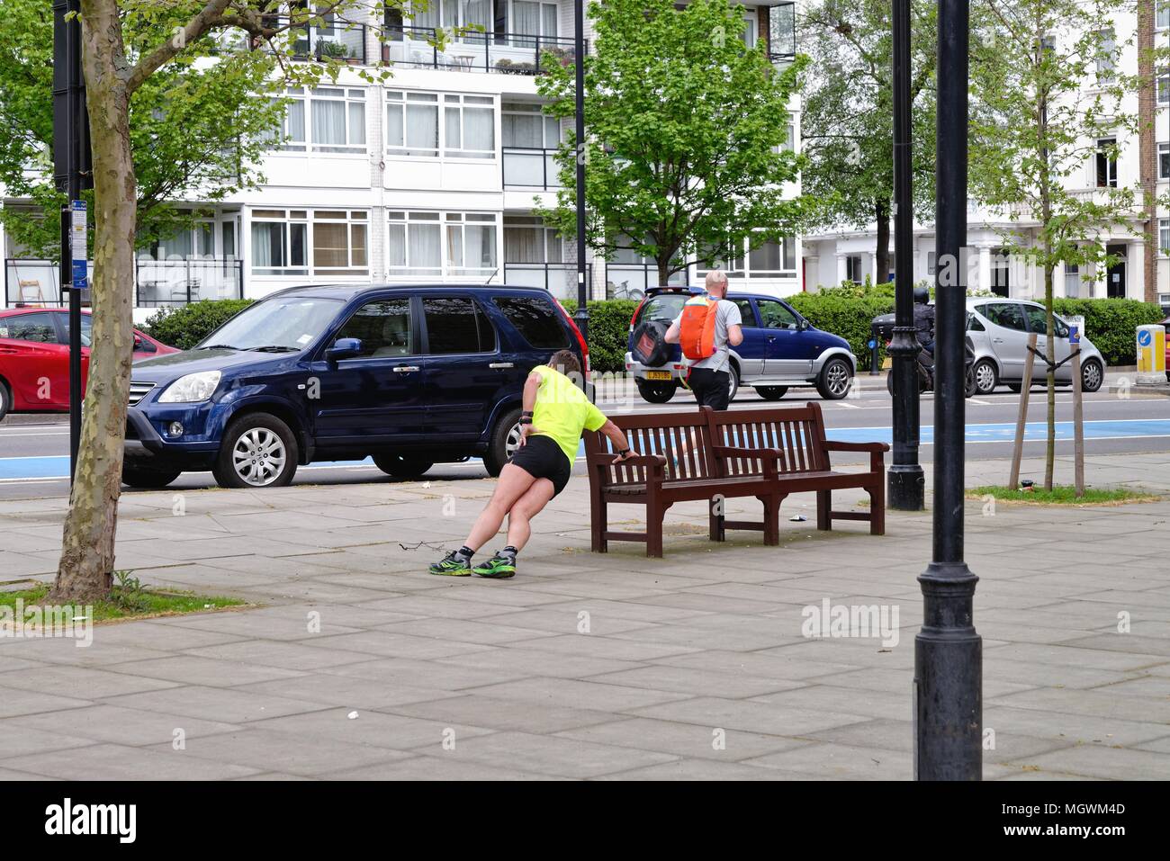 Male Eurasian runner doing side press ups on a wooden street bench in Pimlico London England UK Stock Photo
