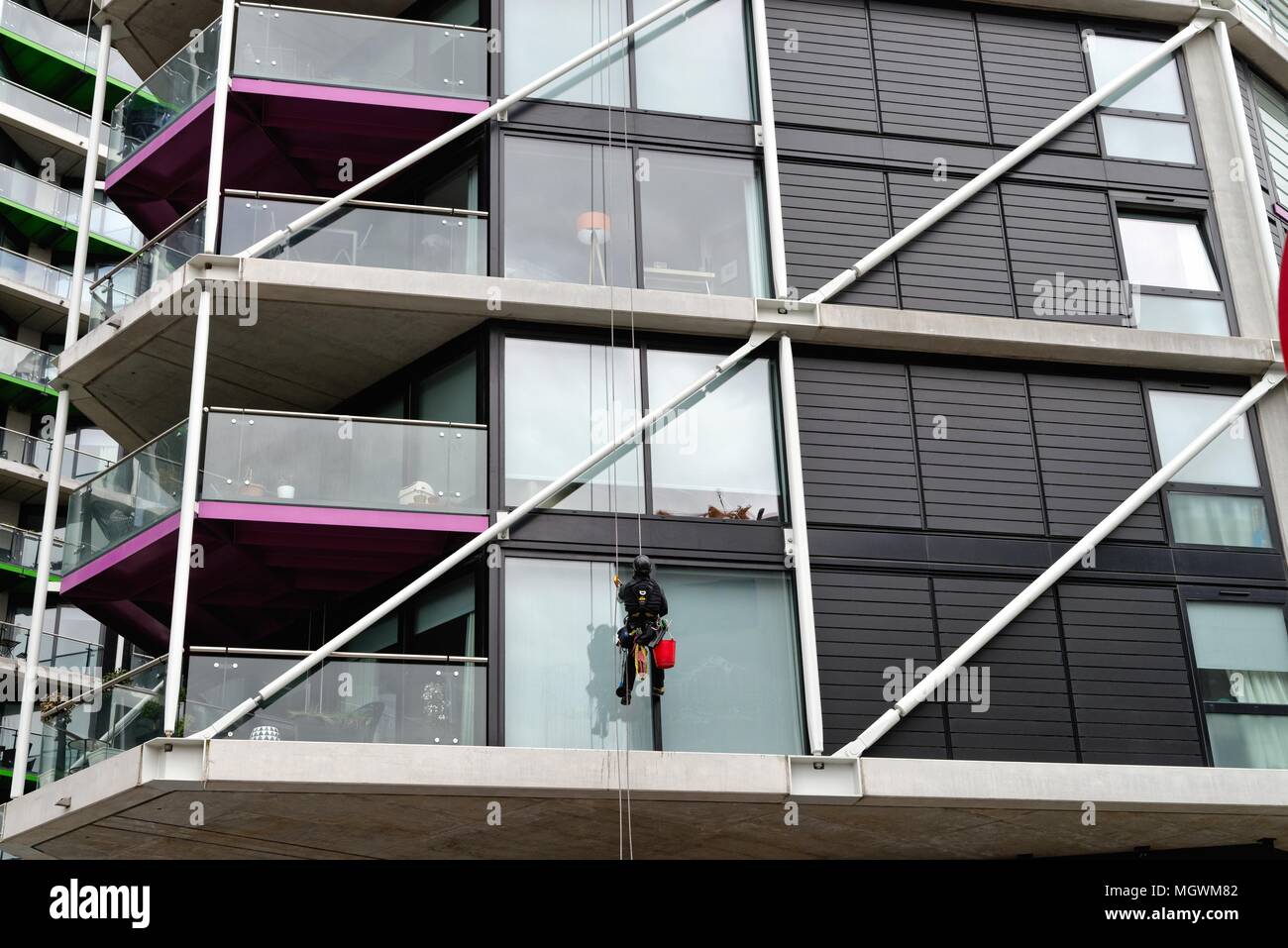 Window cleaner abseiling on modern block of apartments cleaning windows Battersea London England UK Stock Photo