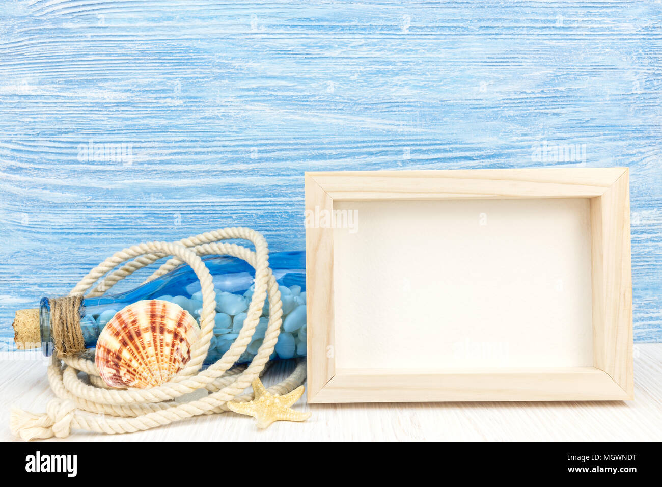 empty photo frame, bottle with seashells, marine knot, rope and starfish on blue wooden boards background  Stock Photo