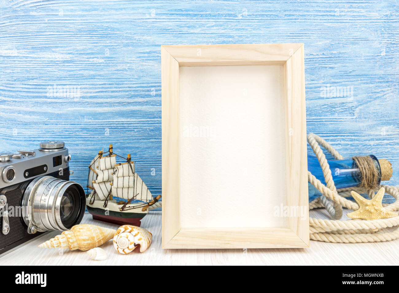 summer holiday background - empty photo frame with classic camera, ship and seashells against blue wooden planks Stock Photo