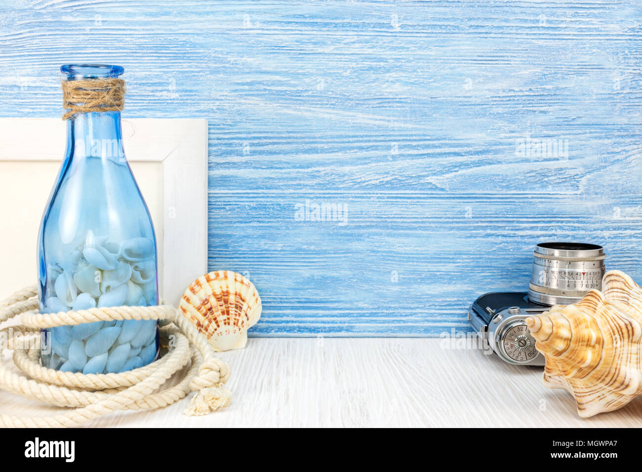 old photo camera, frame, various seashells, marine rope and bottle on blue wooden boards background Stock Photo