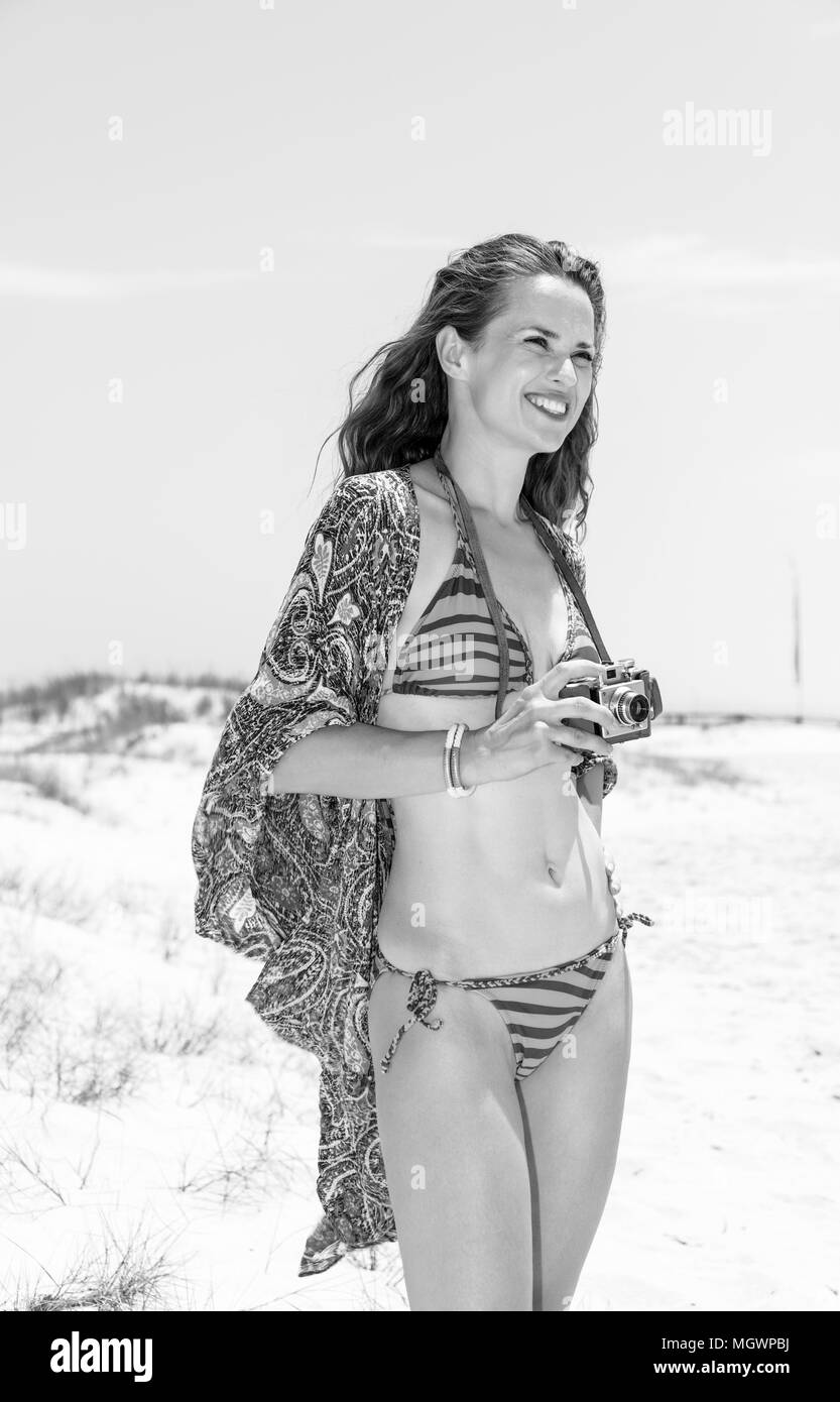 Bohemian vibe vacation. smiling boho young woman in bikini on the seashore with vintage film camera looking into the distance Stock Photo