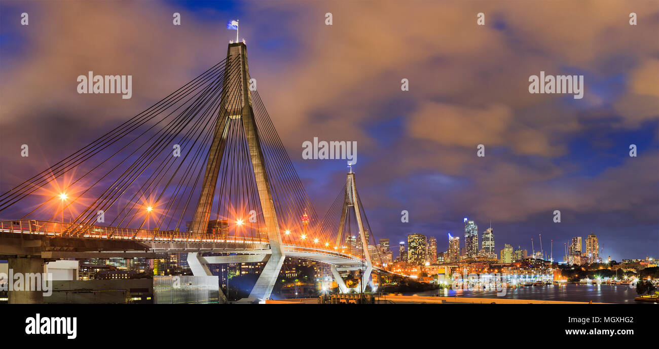 Anzac bridge with flags of Australia and New zeland on top gates with steel cables in front of Sydney city CBD urban towers at sunset with bright illu Stock Photo