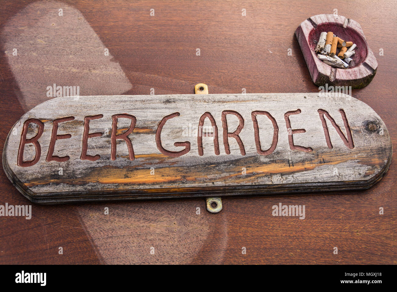 Rustic, weather worn, hand-carved signage for a pub 'beer garden' on wooden table with a wooden ashtray. Could represent the decline of English pubs Stock Photo