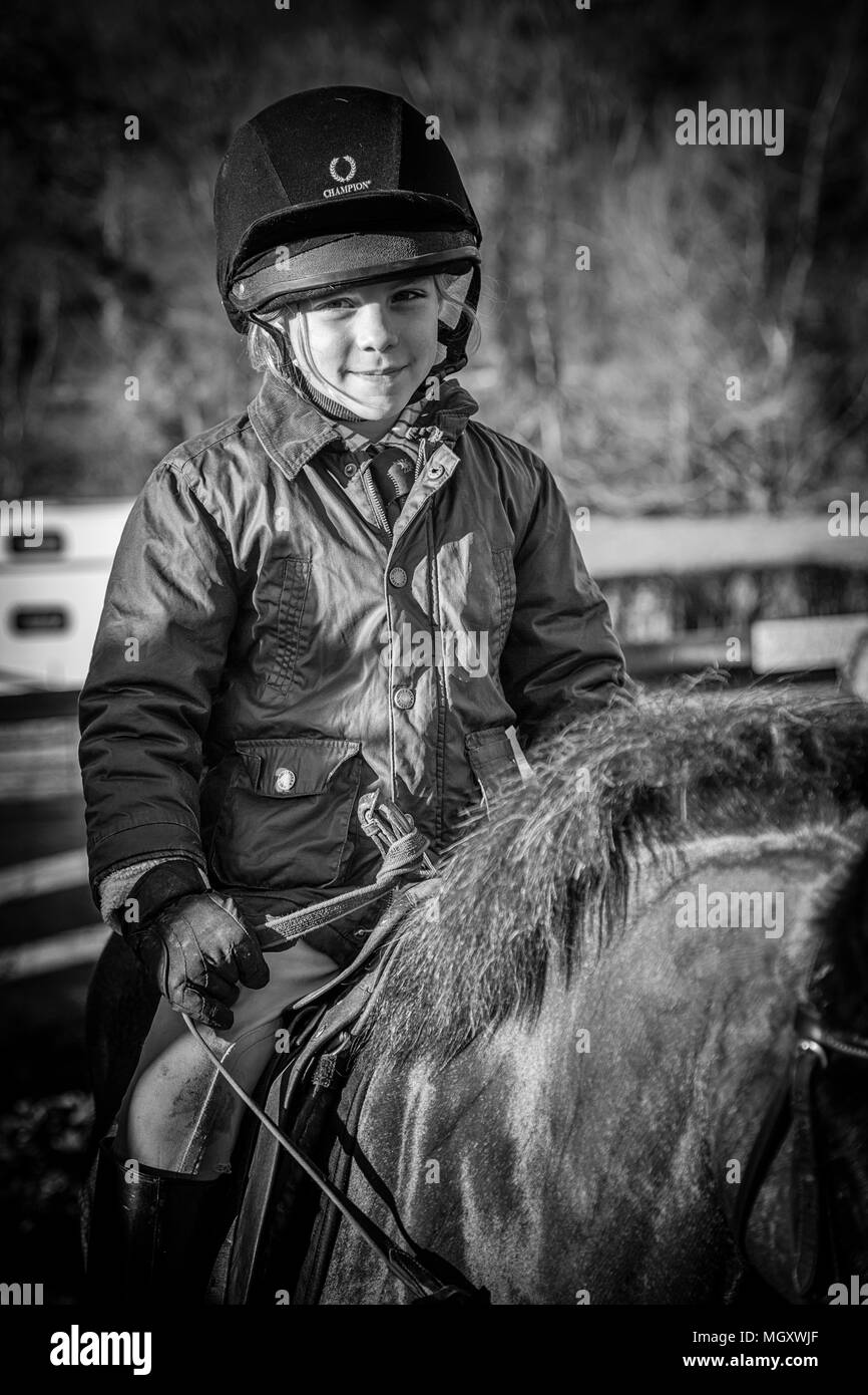young boy sitting on a horse wearing a coat and riding hat in black and white on a sunny morning Stock Photo