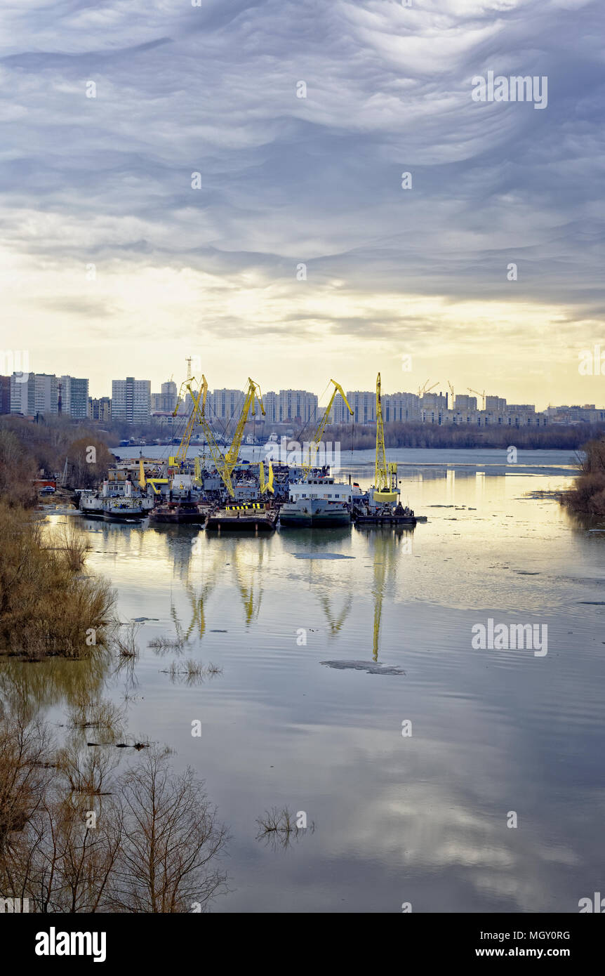 Beginning of navigation on the Irtysh river. Thunder sky .Tugboats, floating cranes and ships parked in a backwater Stock Photo