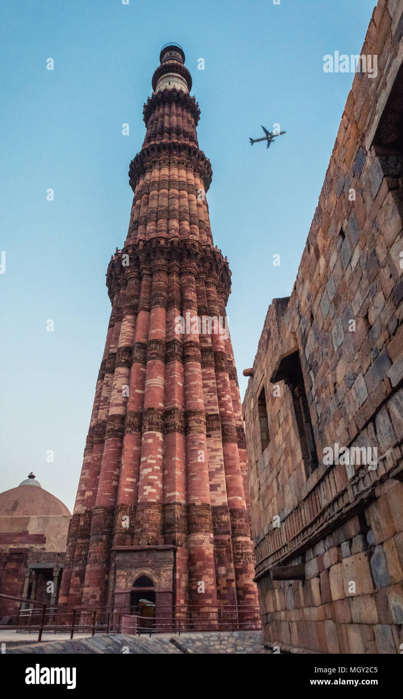 Tiny aeroplane flying across the sky during the blue hour in the Qutub Minar complex, the heritage wonder of New Delhi Stock Photo