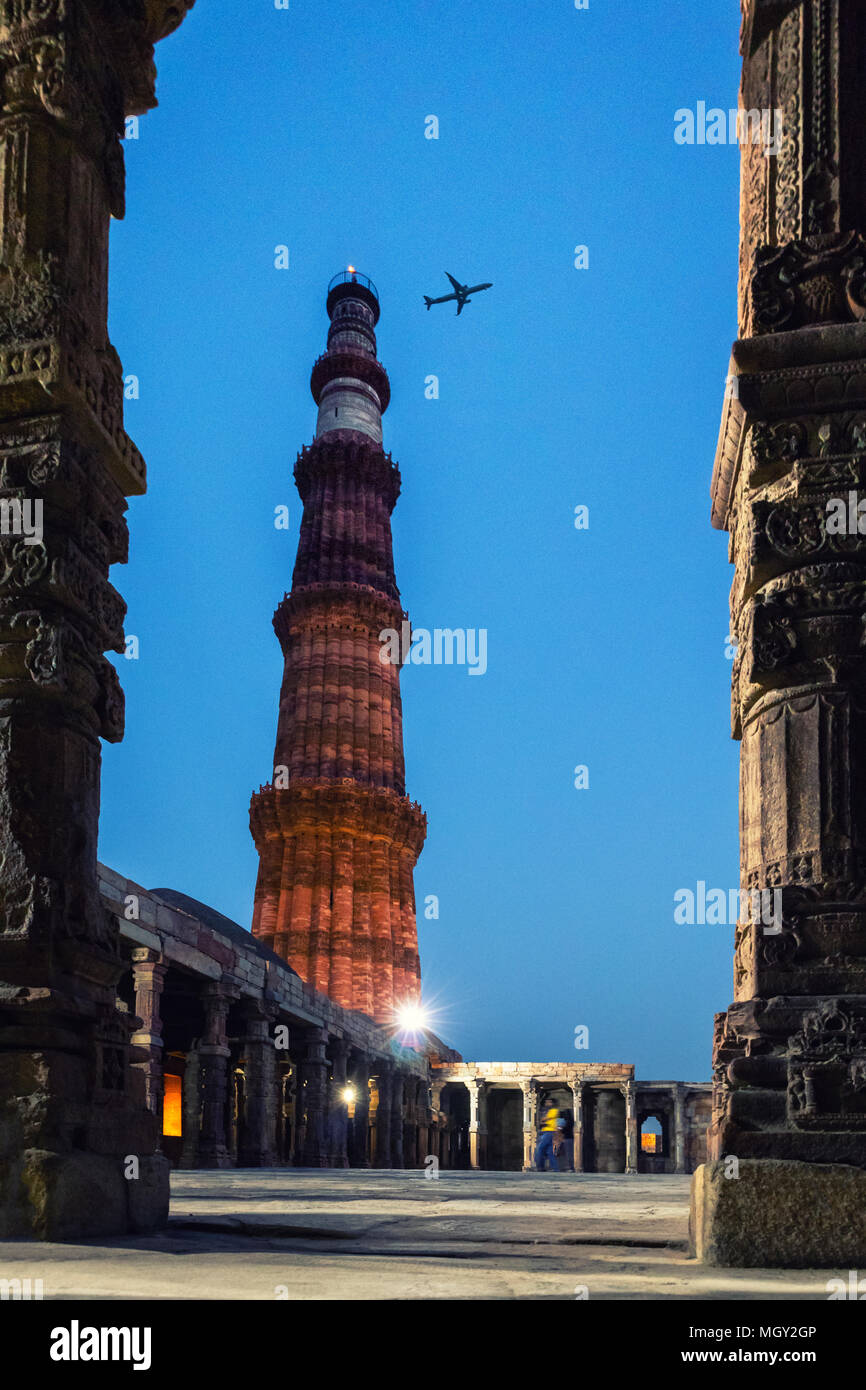 Tiny aeroplane flying across the sky during the blue hour in the Qutub Minar complex, the heritage wonder of New Delhi Stock Photo