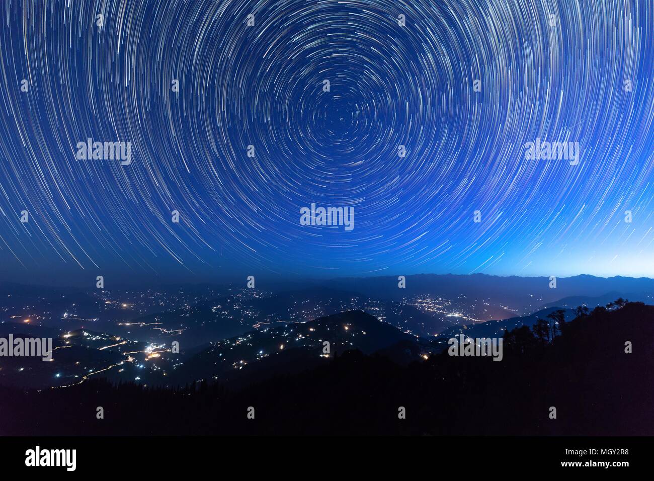 Night sky star trails around the North star with city lights in the background taken from the top of a hill in himalayas Stock Photo