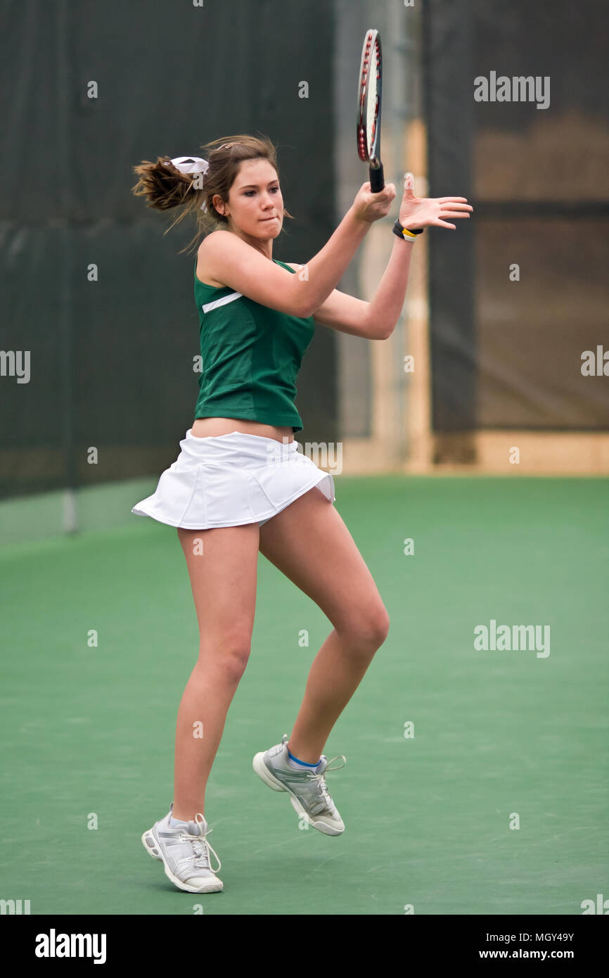 Female high school tennis player executes forehand on follow through