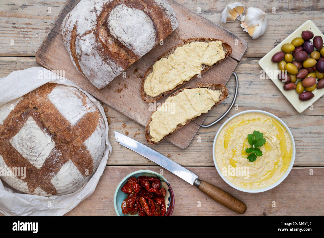 Sourdough bread and spelt sourdough bread with homemade hummus,  olives and sundried tomatoes on a bread board. UK Stock Photo