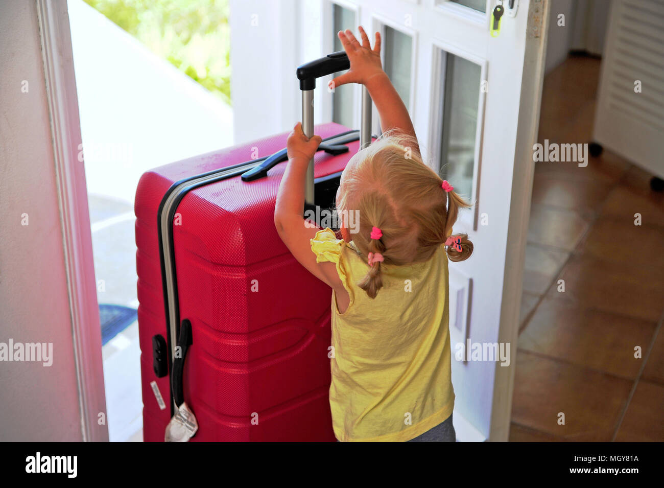 Little girl holding big suitcase at opened door Stock Photo