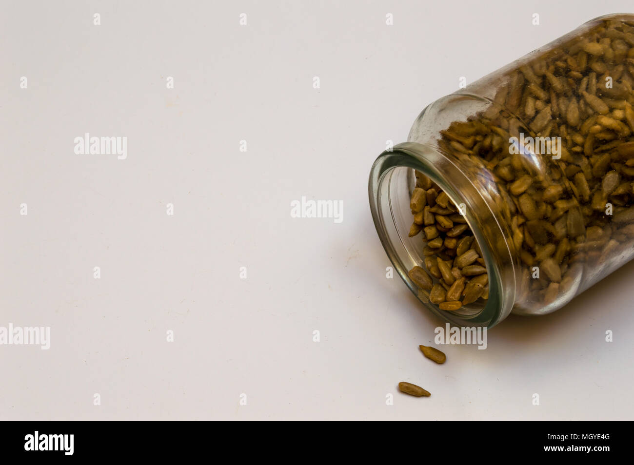 Vintage glass jar filled with peeled sunflower seeds and spilled. Food isolated on white background with space to ad text or elements. Stock Photo