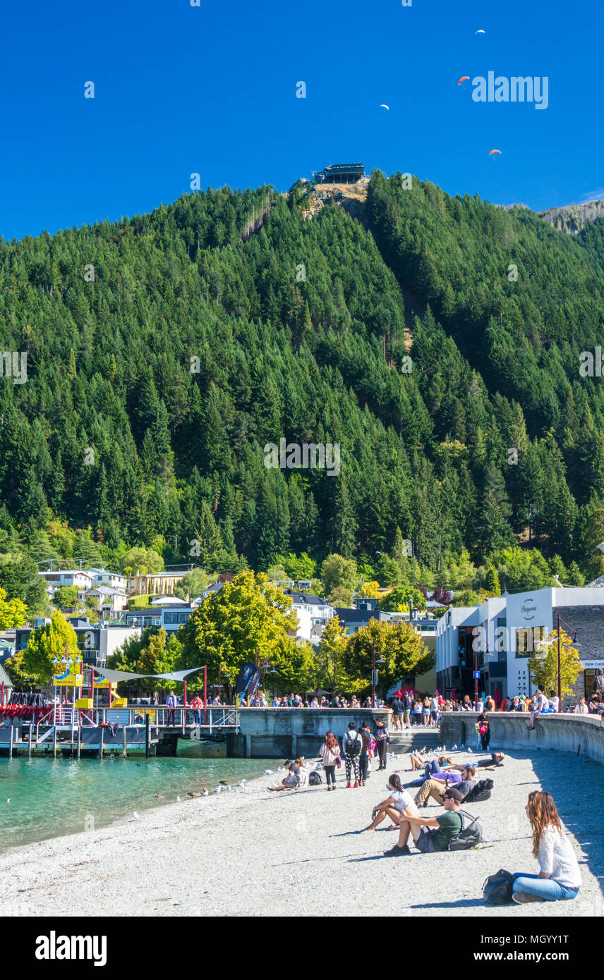 view of the queenstown skyline gondola queenstown hill from the sandy beach on lake wakatipu shore lakeside queenstown South Island New Zealand nz Stock Photo