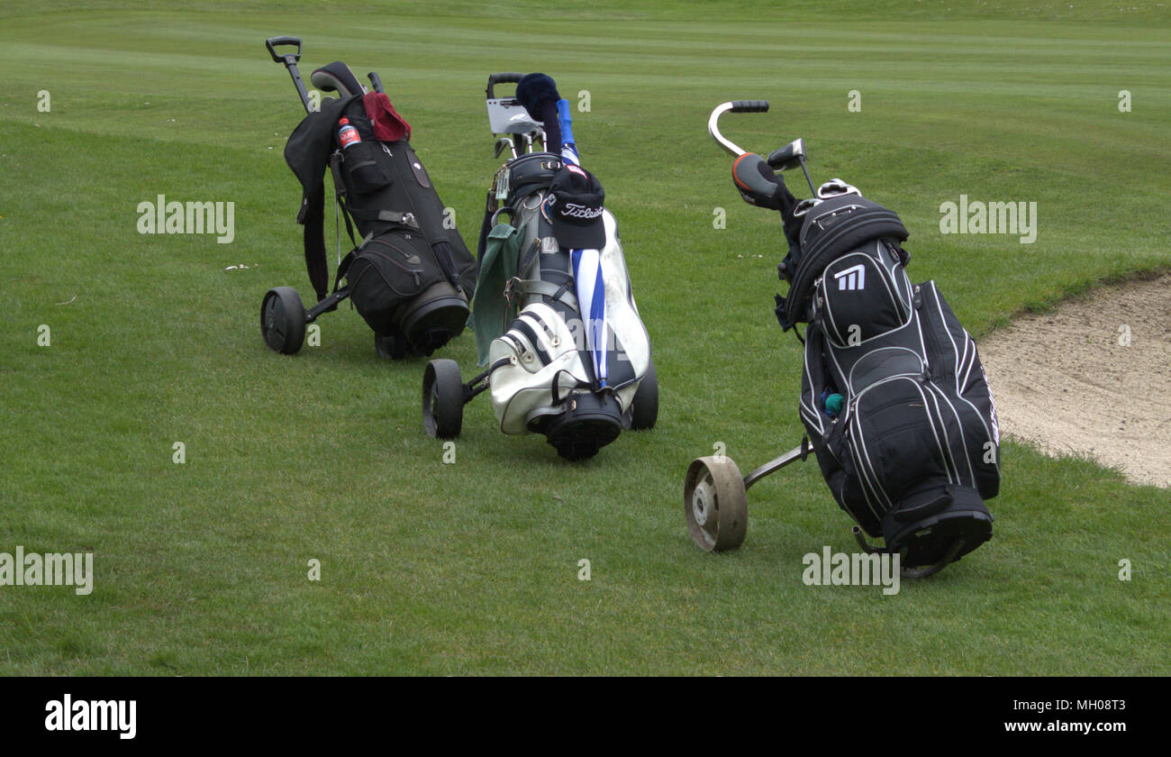 3 golf bags left in a line beside a sand bunker on the fairway of a golf course. Stock Photo