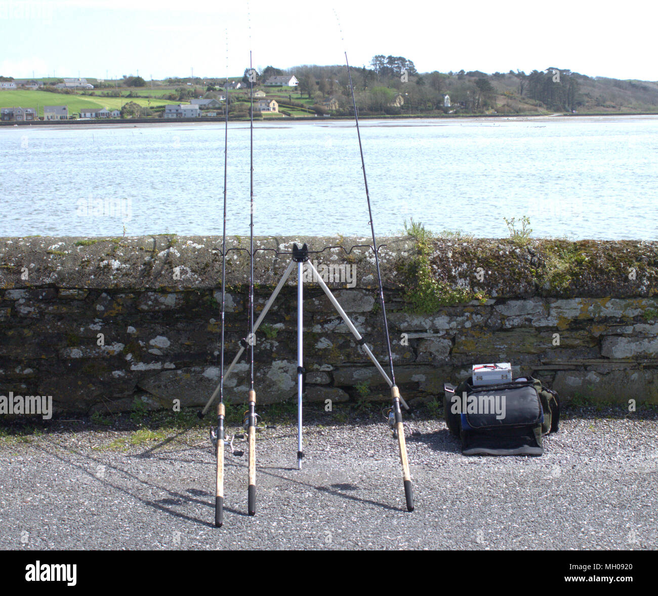 3 three fishing rods on a 4 rod rest sea fishing over a sea wall, on a bright spring morning with fishing tackle bag close by. Coastline Ireland Stock Photo