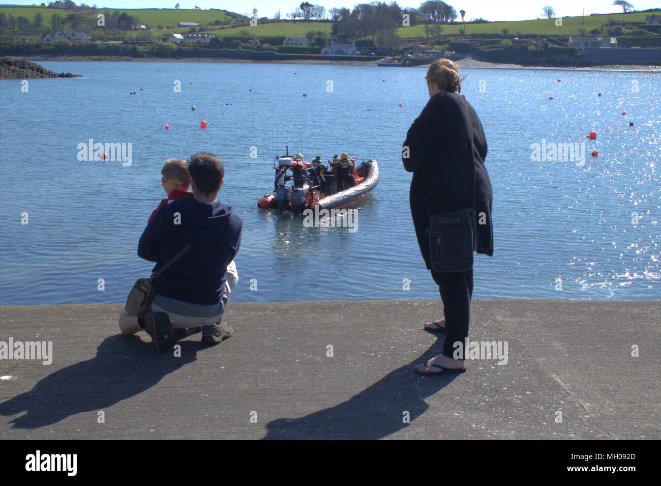 family couple on holiday with a small boy watching the irish coastguard rescue boat being launched from the end of a jetty in ireland. Stock Photo