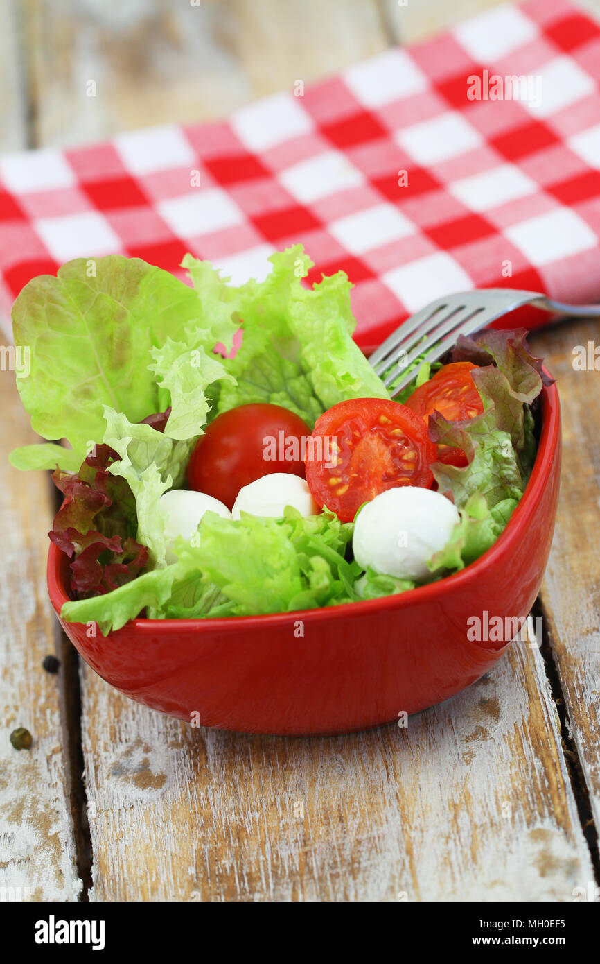 Bowl of fresh mozzarella salad with lettuce and cherry tomatoes on wooden surface close up Stock Photo