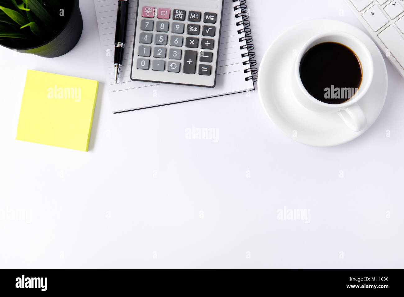 White office desk table with keyboard, notepad, pen, cup of coffee and plant. Stock Photo