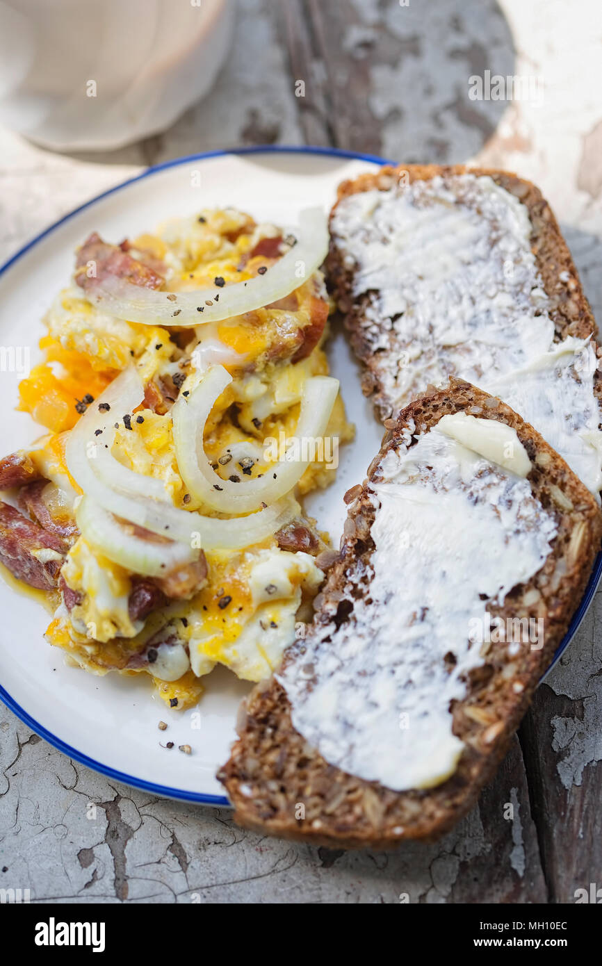 Scrambled eggs with bacon, sausage and onion with wholegrain bread and coffee Stock Photo