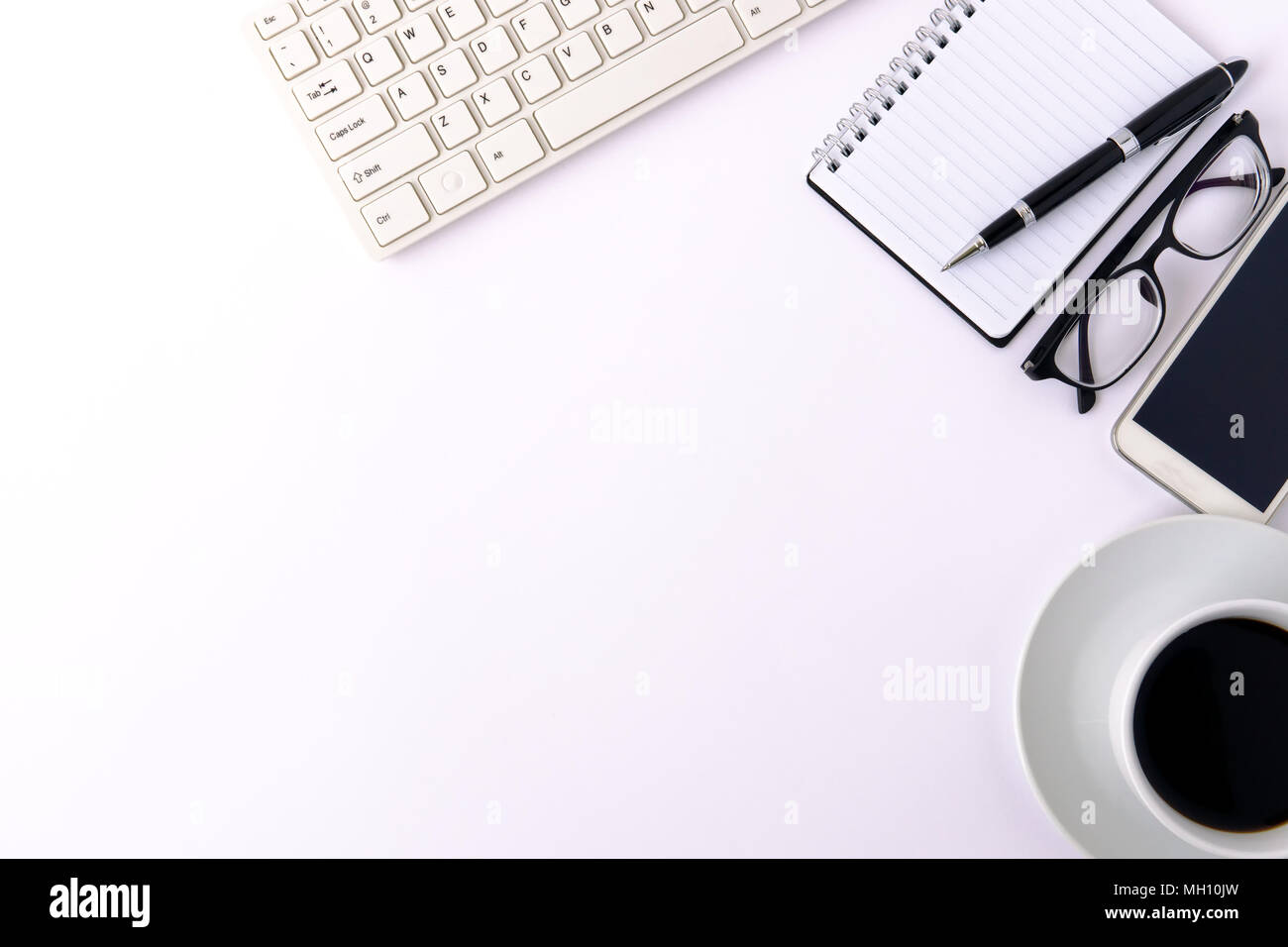 White designer office desk table with blank notebook page with smartphone, pen, computer keyboard, eyeglasses and cup of coffee. Top view, flat lay. Stock Photo