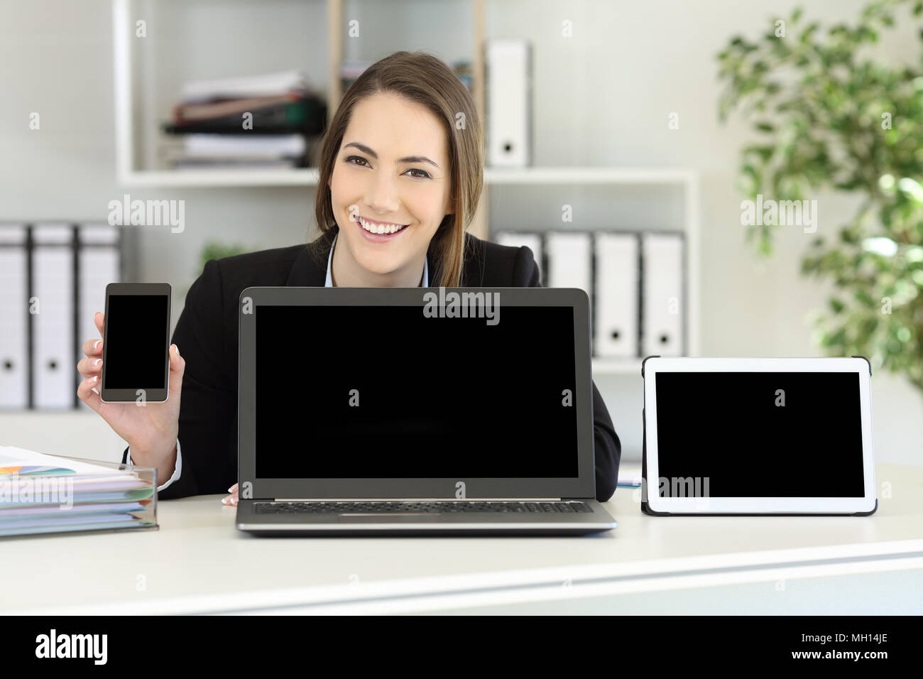 Happy office worker showing multiple device blank screens on a desktop Stock Photo